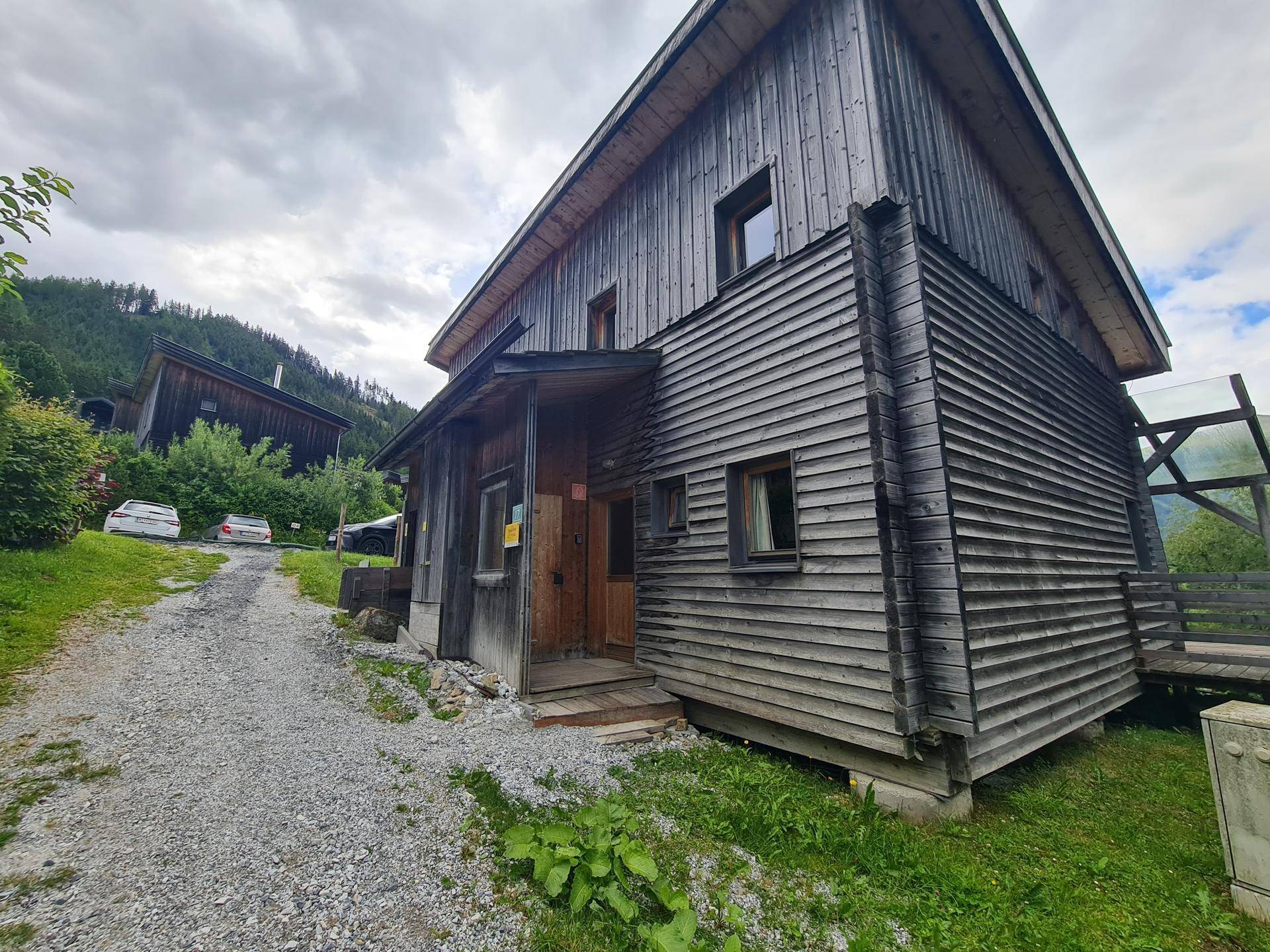 Rustikales Holzhaus mit traditioneller Fassade und Schotterweg in ländlicher Umgebung.