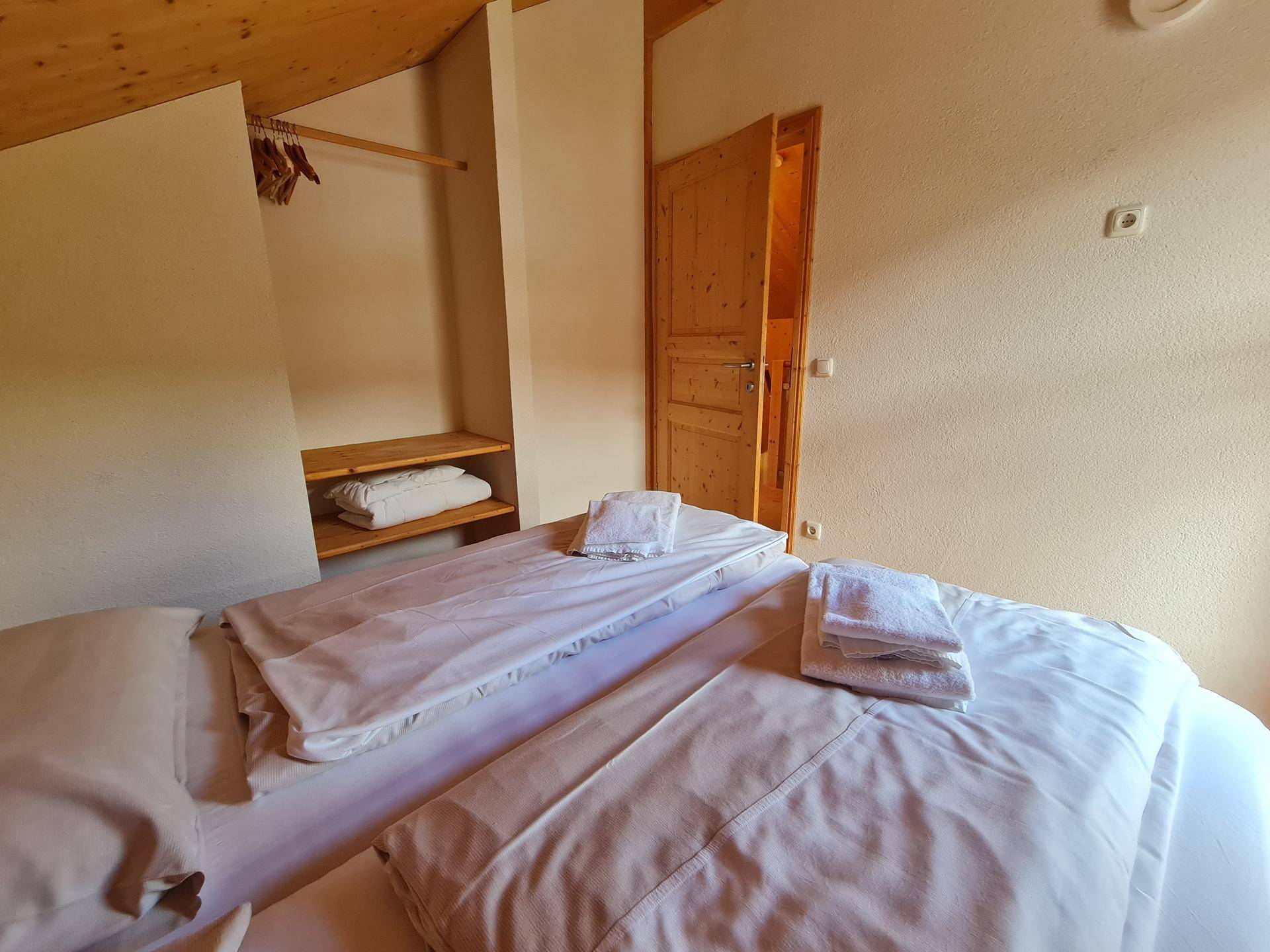 Schlafzimmer im Dachgeschoss mit Holzboden, Holzwänden und offenem Kleiderschrankbereich.