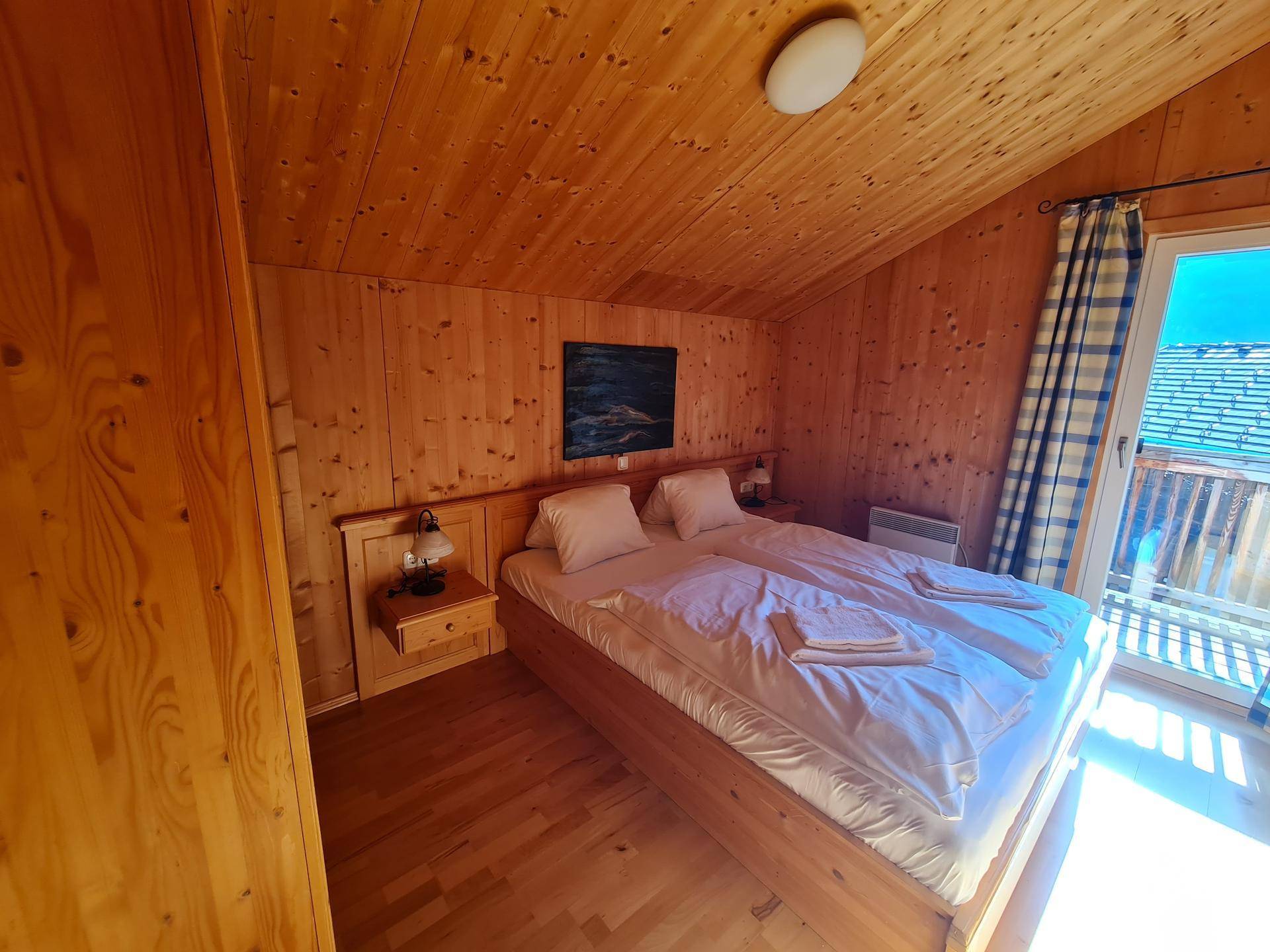 Helles Schlafzimmer mit Holzwänden, Holzboden und Balkonzugang.