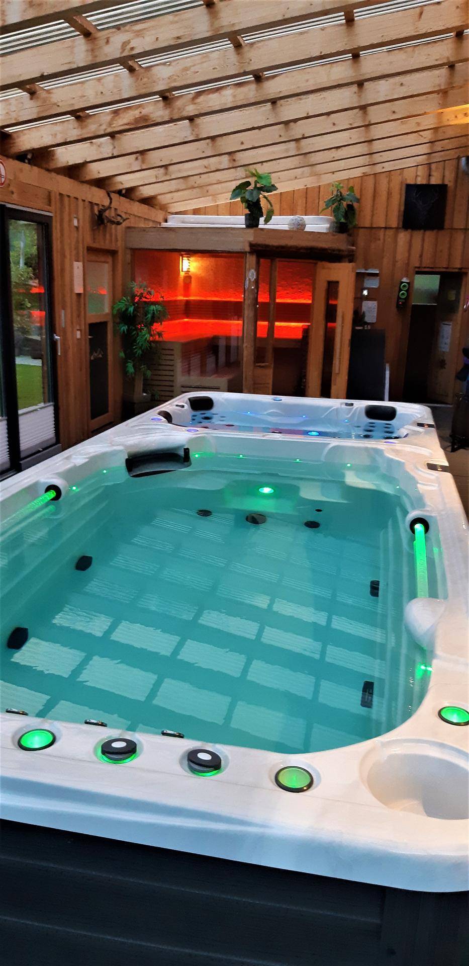 Luxuriöser Wellnessbereich mit großem Whirlpool und sichtbarer Sauna im Hintergrund.