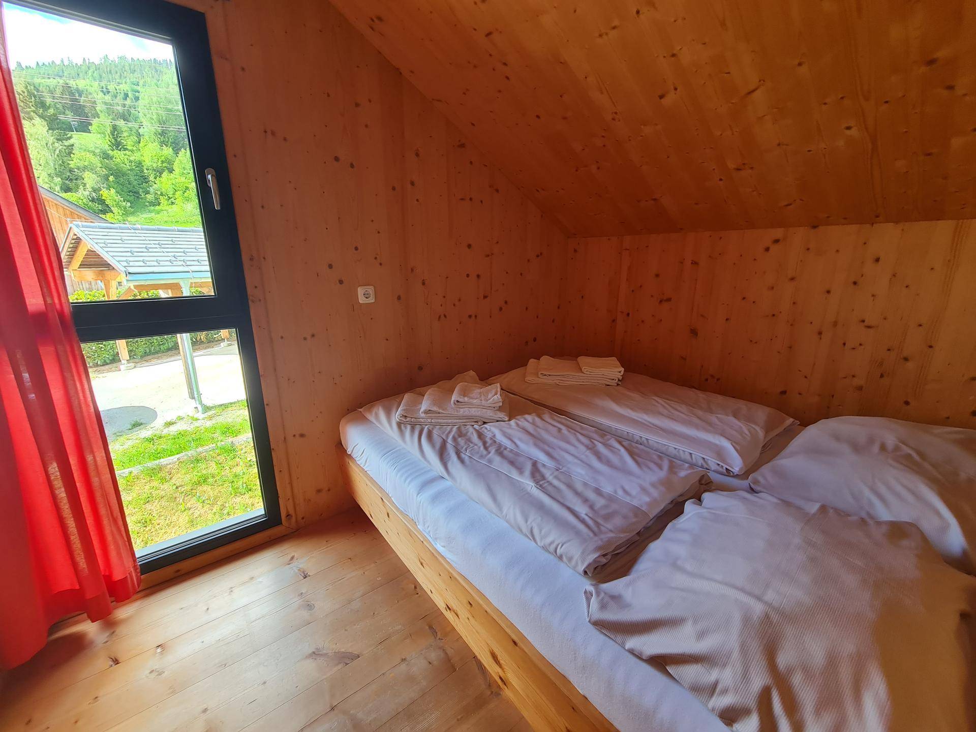 Schlafzimmer im Dachgeschoss mit Holzwänden, Doppelbett und Fensterblick ins Grüne.