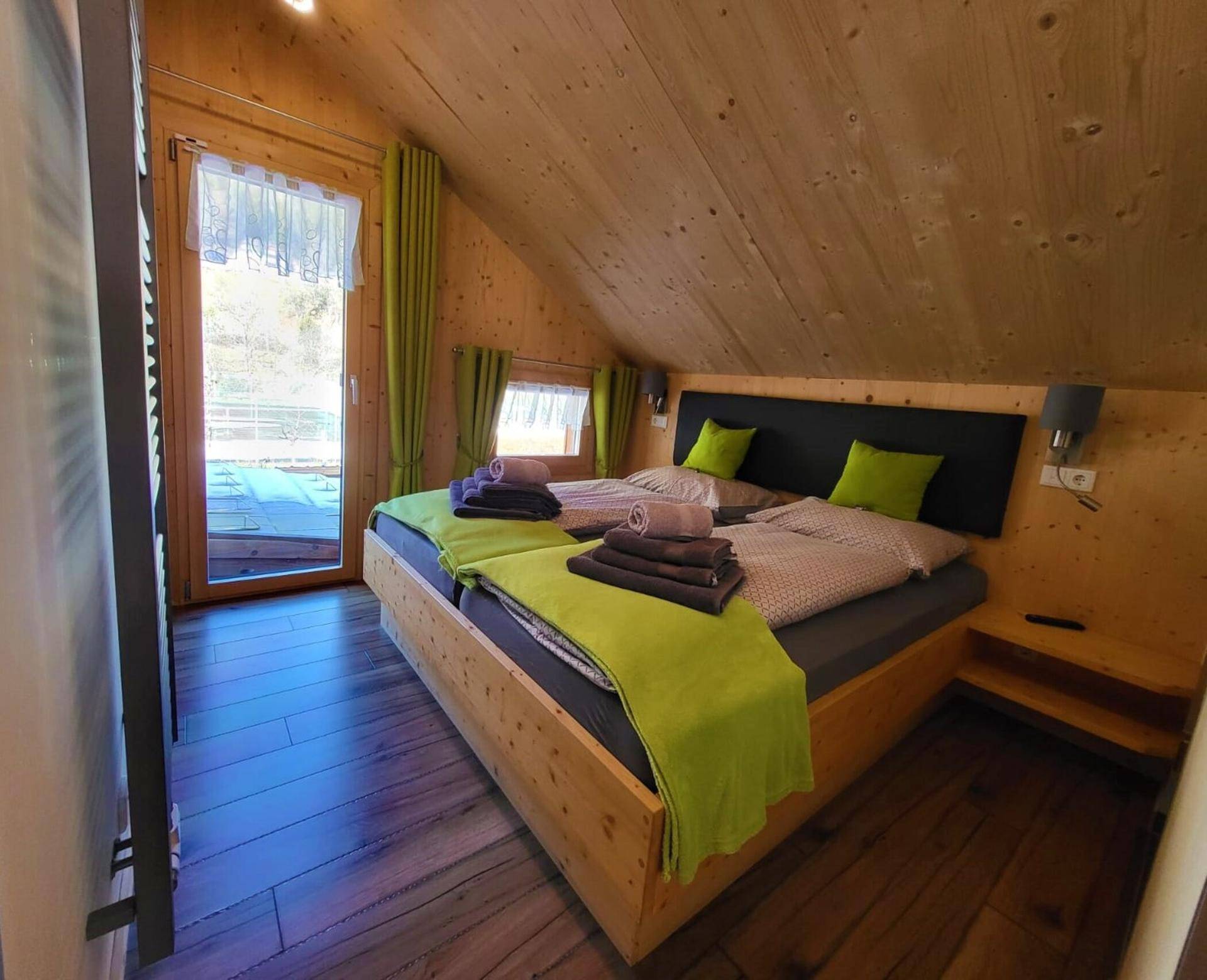 Helles Schlafzimmer im Dachgeschoss mit Holzwänden, Doppelbett und Balkonzugang.