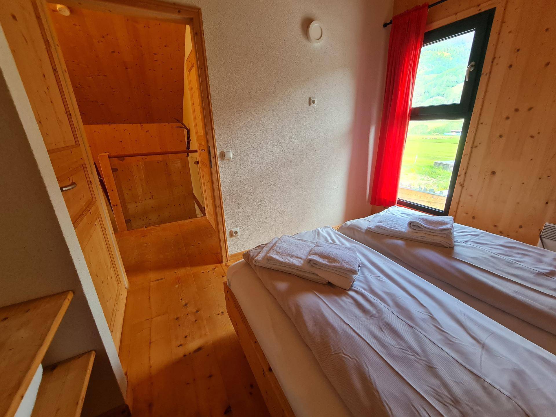 Schlafzimmer mit Holzboden, Holzwänden und Fenster mit Blick auf die grüne Landschaft.