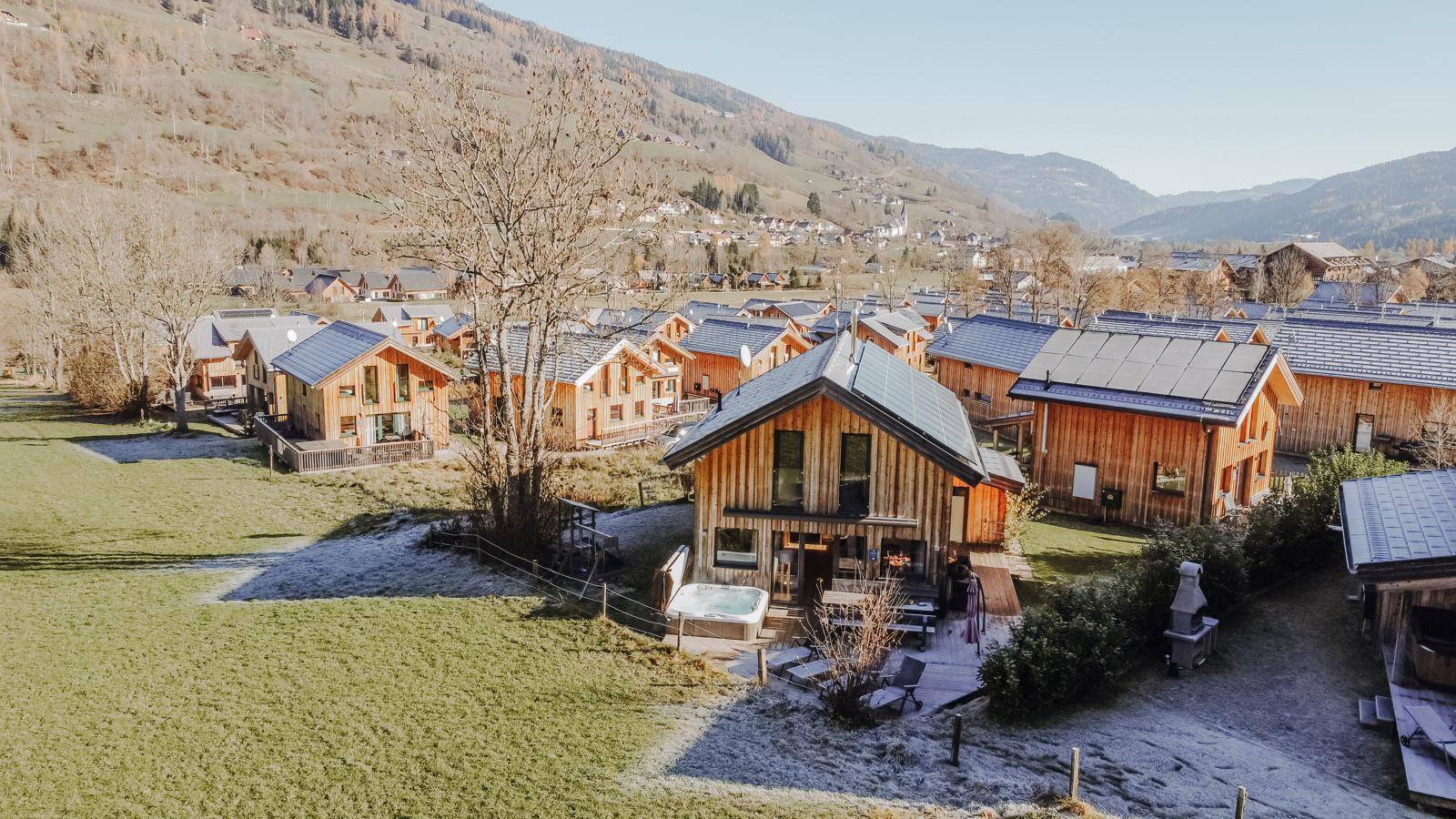 Luftaufnahme einer Siedlung von Holzhäusern in einer ländlichen Umgebung mit Bergen im Hintergrund.