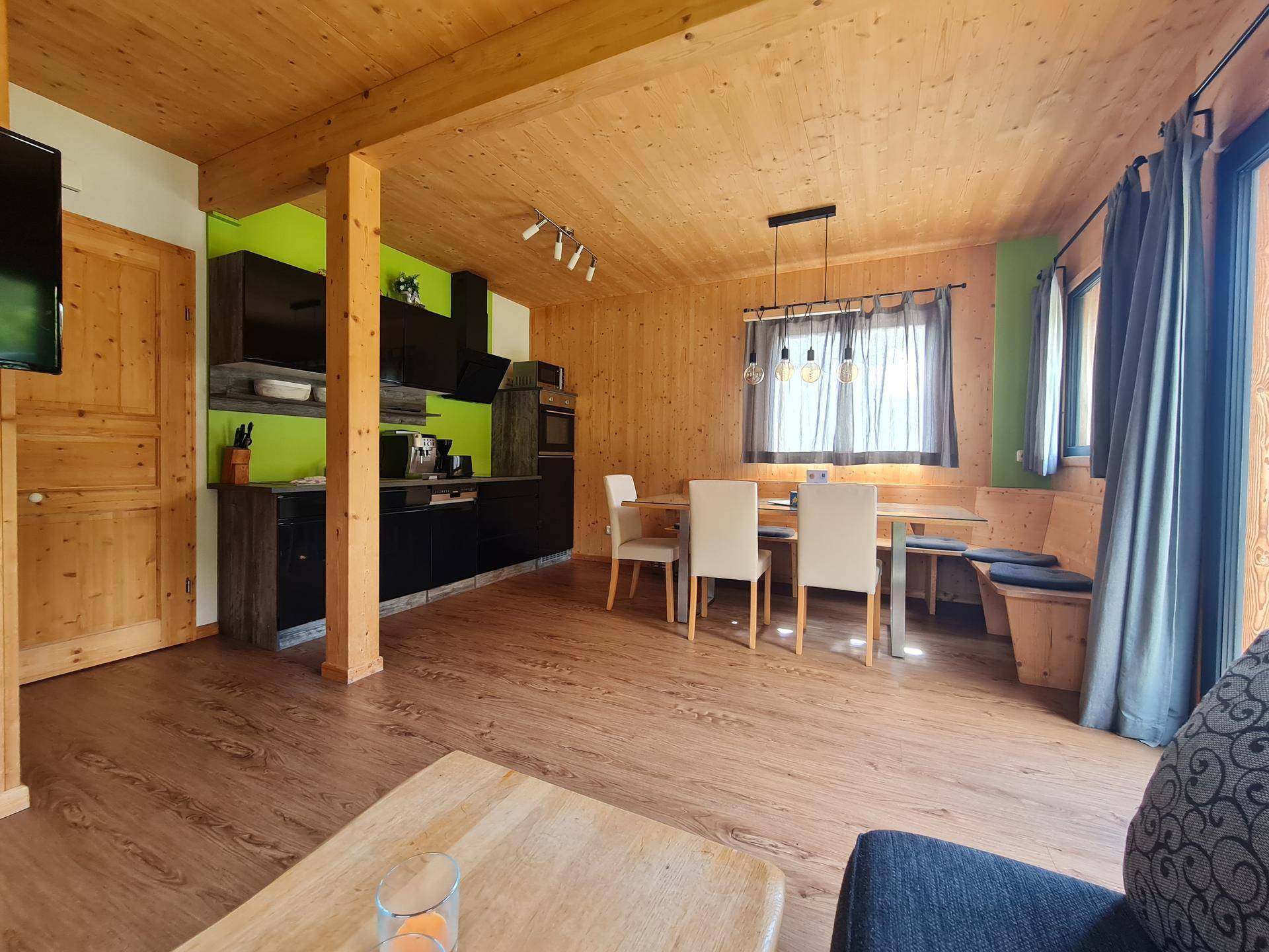 Offener Wohn- und Essbereich mit Holzbalken, moderner Küche und Laminatboden in alpinem Stil.