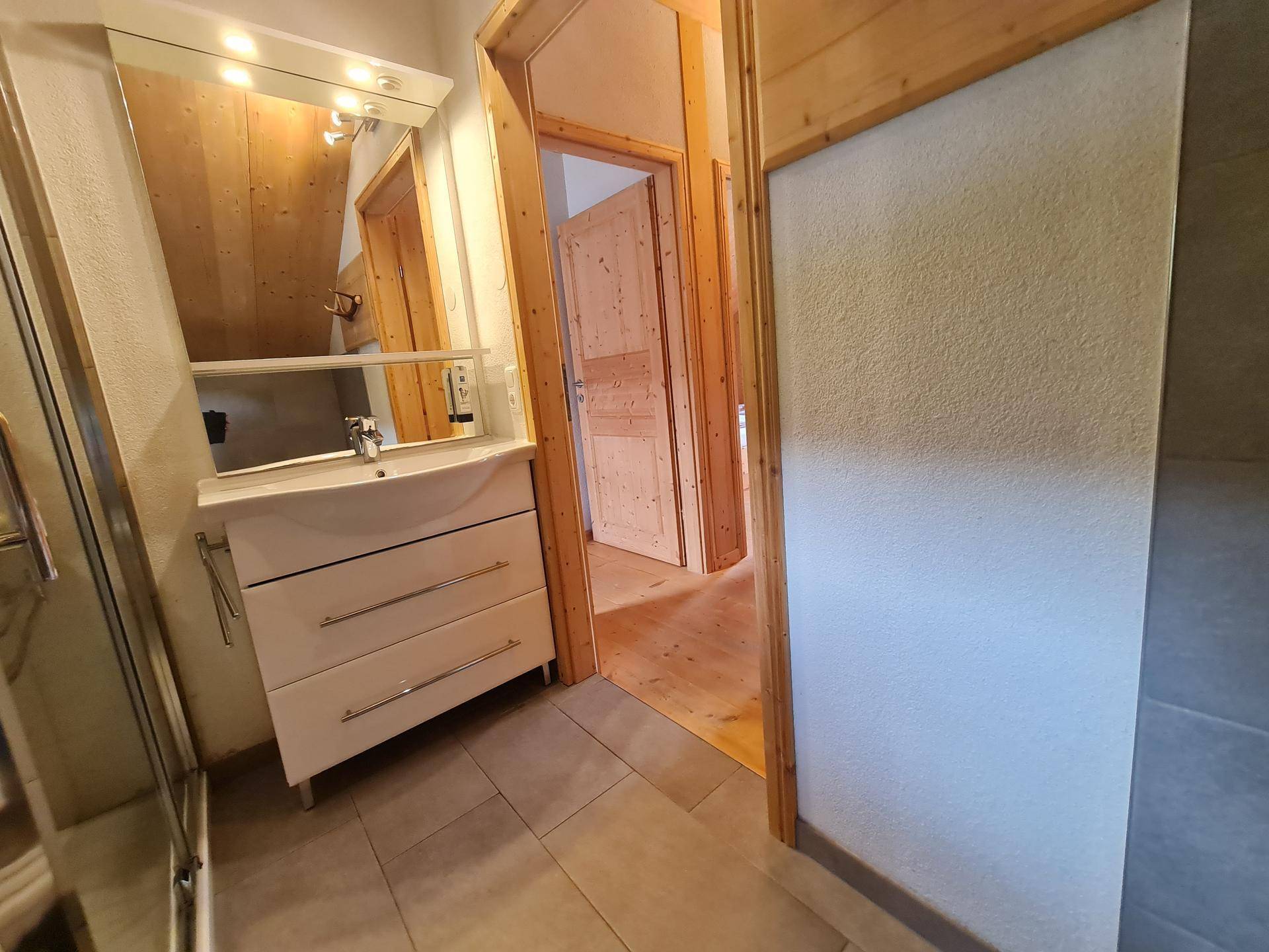 Badezimmer mit Waschtisch, Spiegel und Zugang zu einem weiteren Raum.