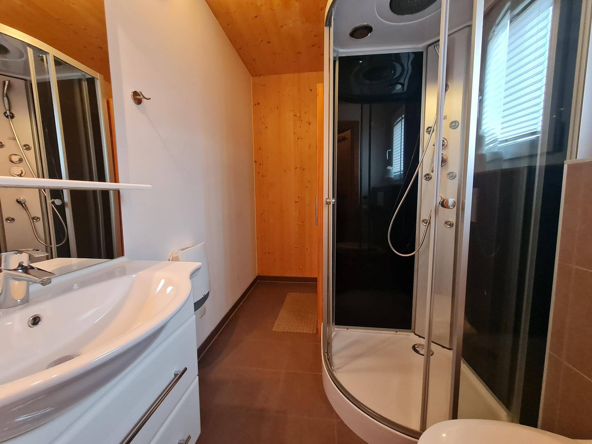 Badezimmer mit Duschkabine, Waschbecken und dunklen Bodenfliesen.