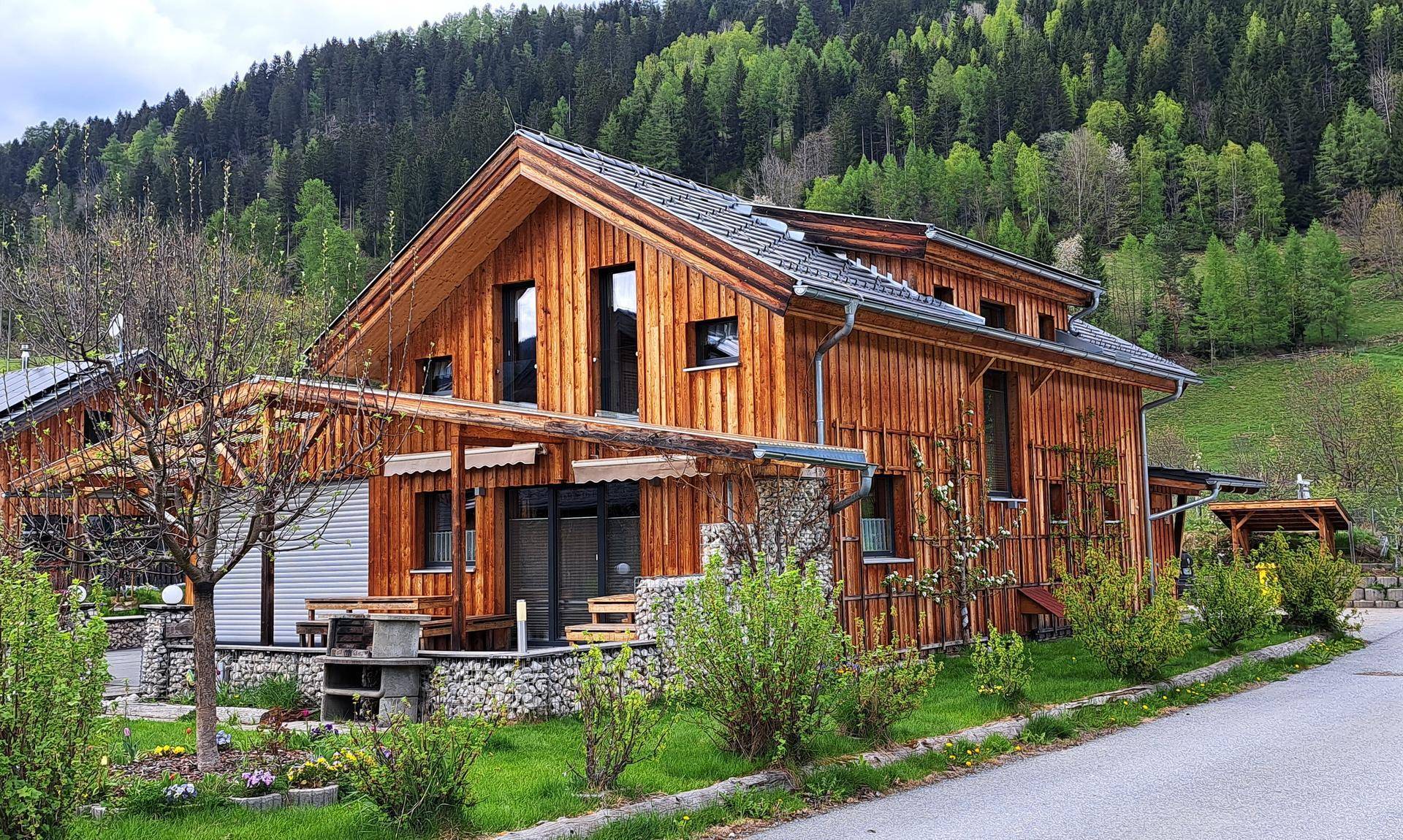 Attraktives Holzhaus mit Satteldach, umgeben von grüner Natur und einem gepflegten Garten.