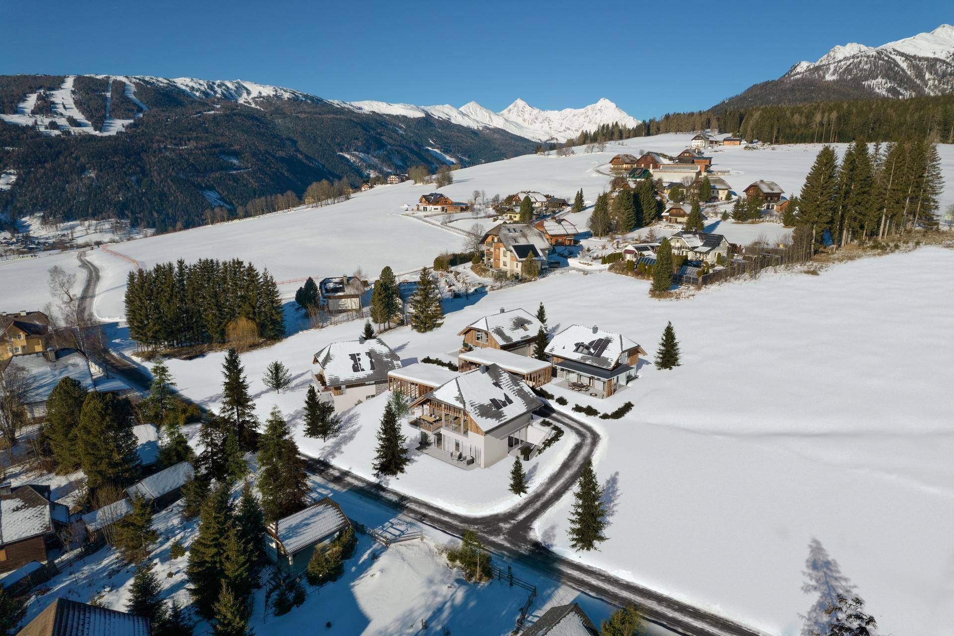 Panoramablick auf eine Gruppe von Häusern in einer verschneiten Berglandschaft mit weiten Ausblicken.