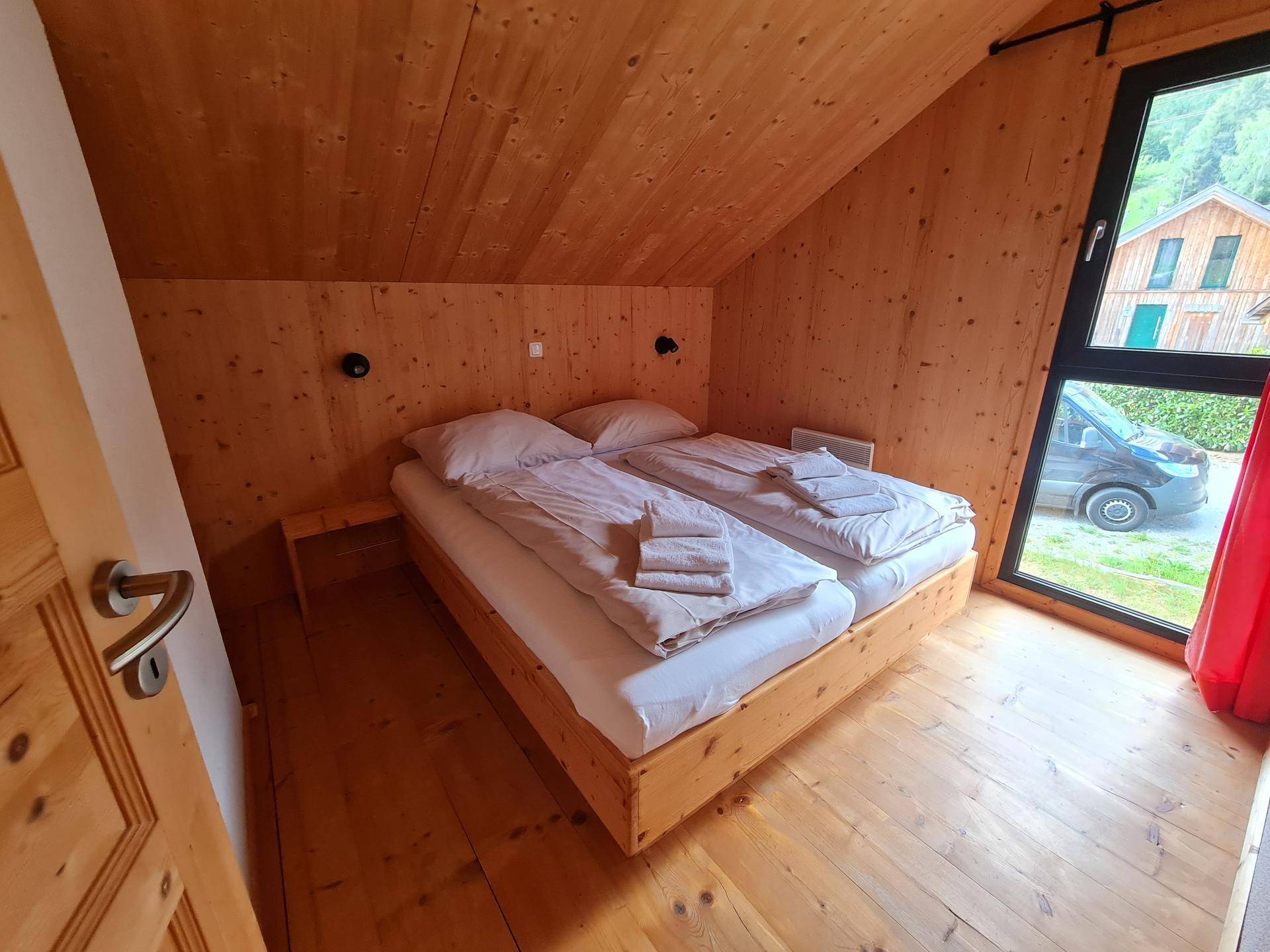 Helles Schlafzimmer mit Doppelbett, Holzboden und Fenster mit Blick nach draußen.