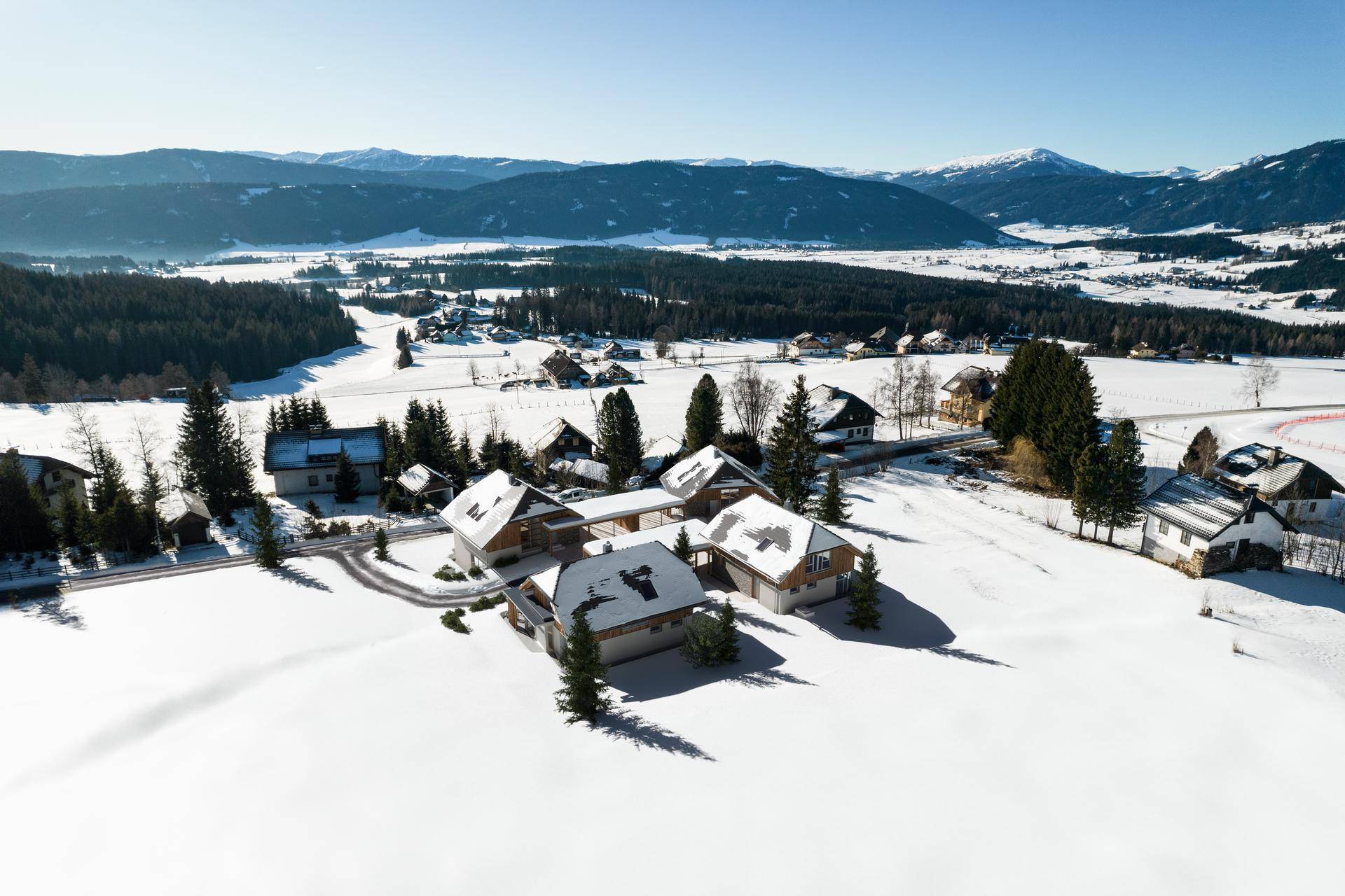 Luftaufnahme einer verschneiten Siedlung in einem Tal mit weitem Blick auf die umliegende Berglandschaft.