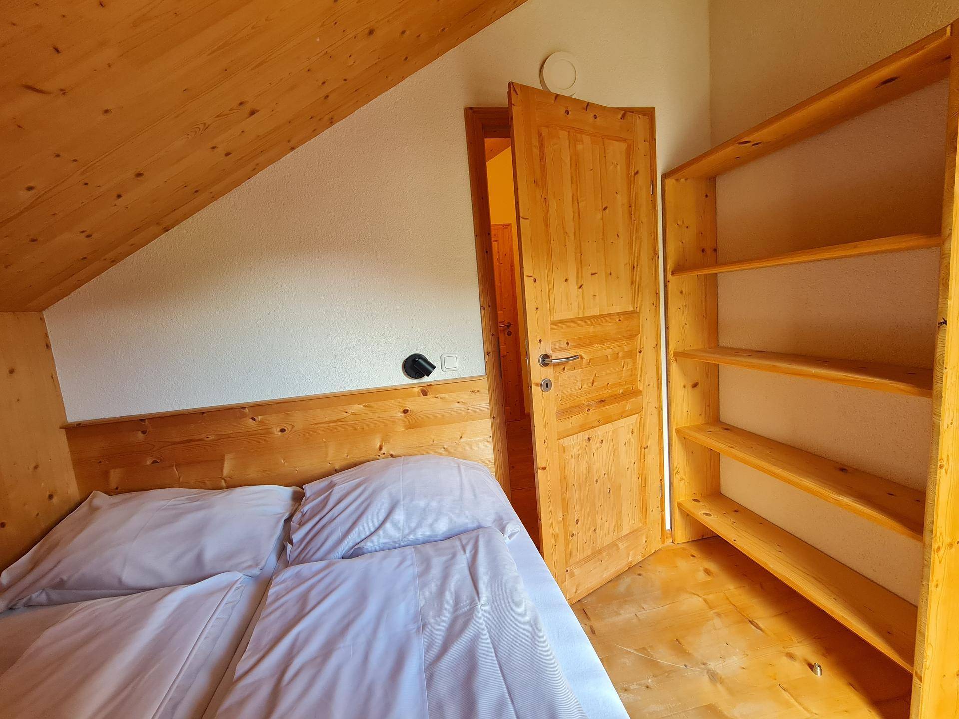 Gemütliches Schlafzimmer mit Holzbett, Regal und schrägen Wänden im Dachgeschoss.