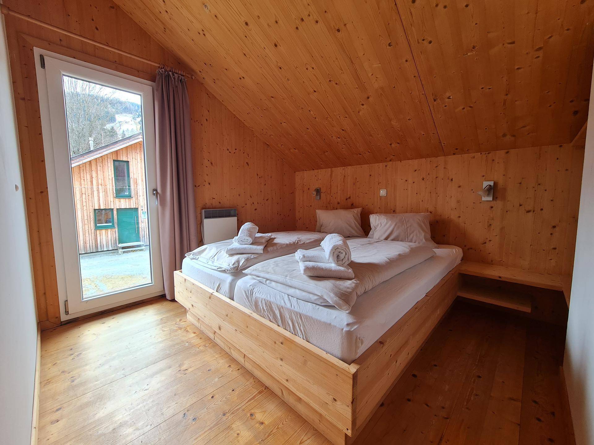 Helles Schlafzimmer mit Doppelbett, Holzvertäfelung und Fenster mit Blick nach draußen.