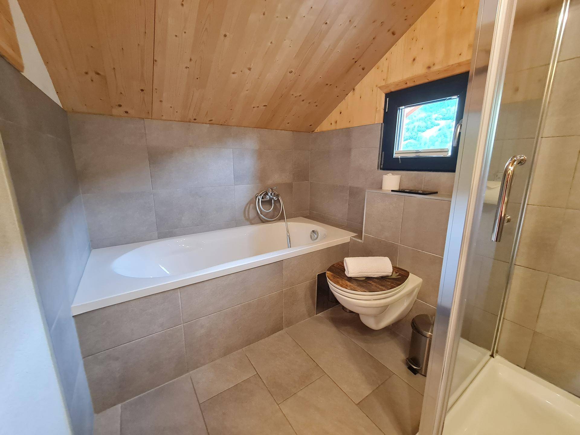 Badezimmer im Dachgeschoss mit Badewanne, Dusche und Fenster mit Bergblick.