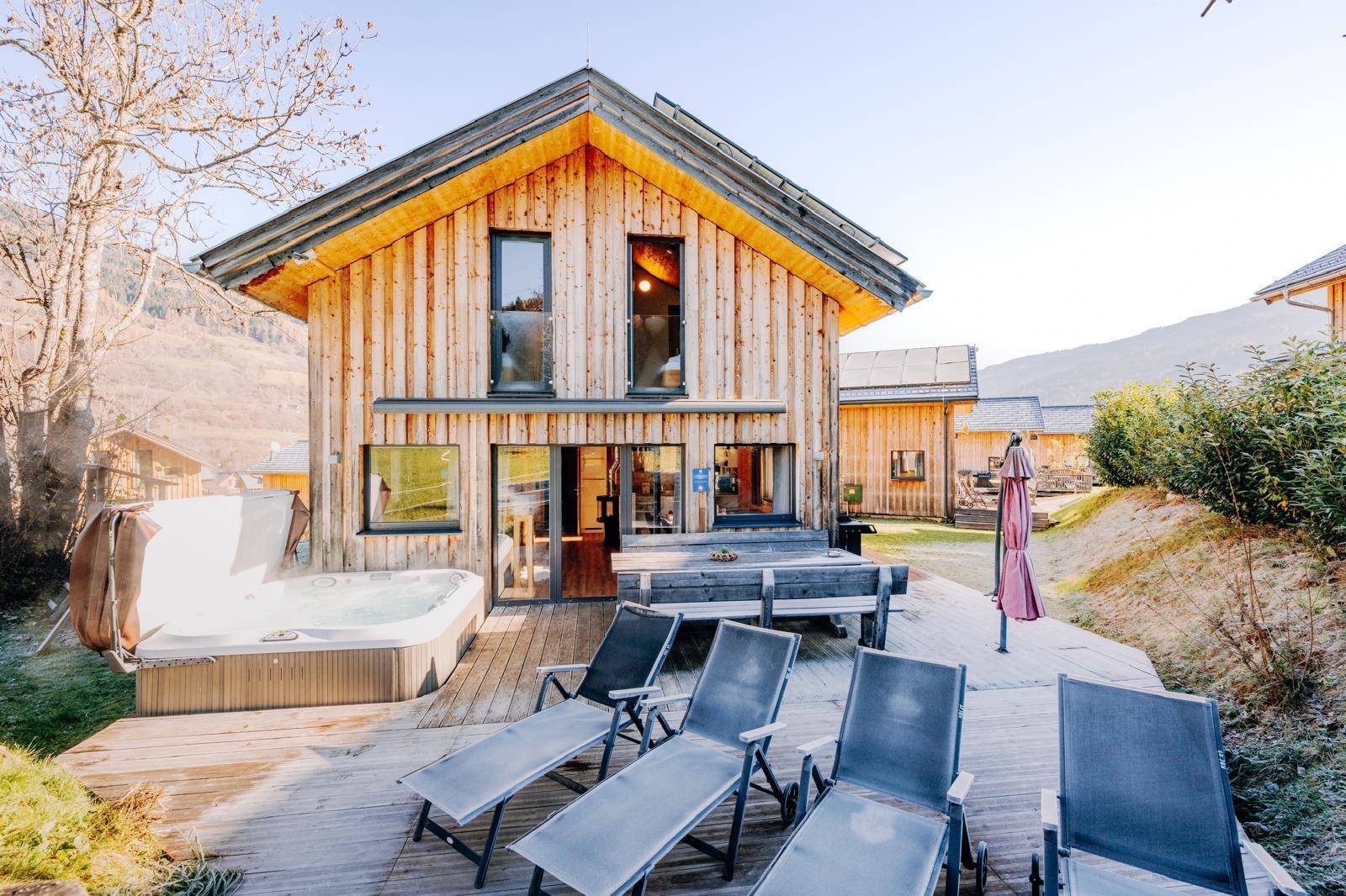 Geräumige Holzterrasse mit Whirlpool und Liegestühlen vor dem modernen Holzhaus.