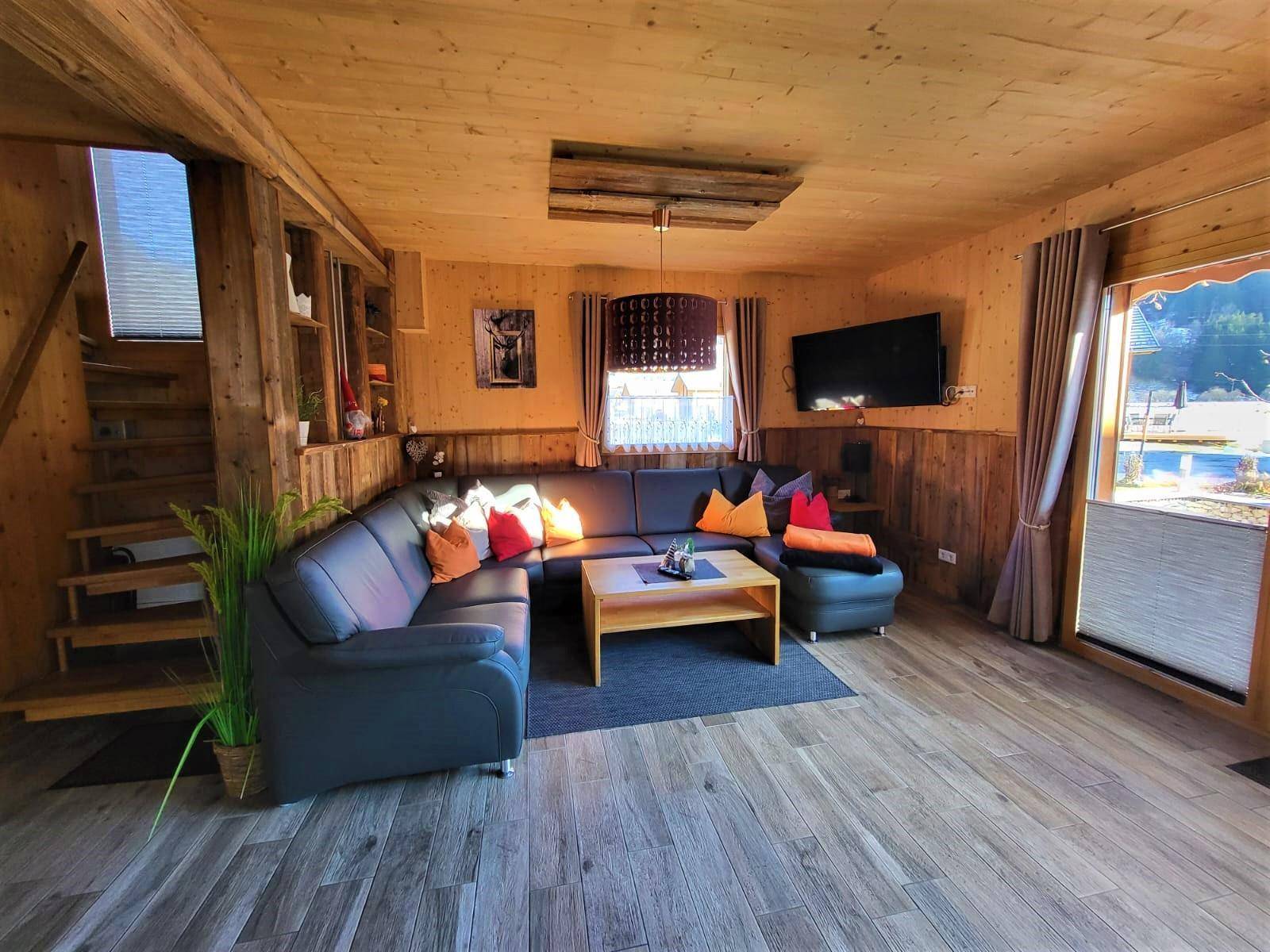 Geräumiges Wohnzimmer mit Holzböden und -wänden, großer Eckcouch und Zugang zur Terrasse.