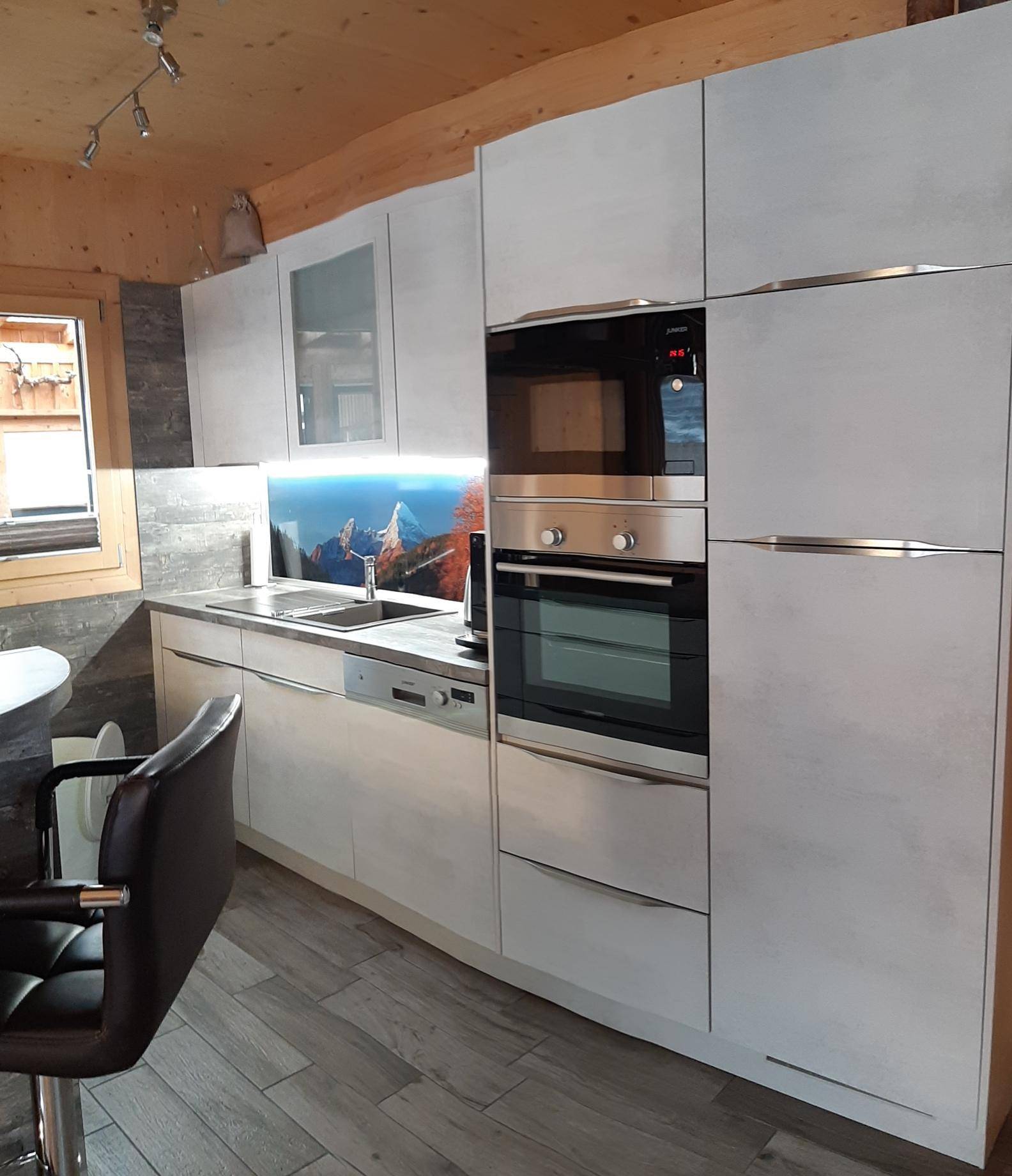 Moderne Einbauküche mit hellgrauen Fronten, integrierten Geräten und Holzwänden.