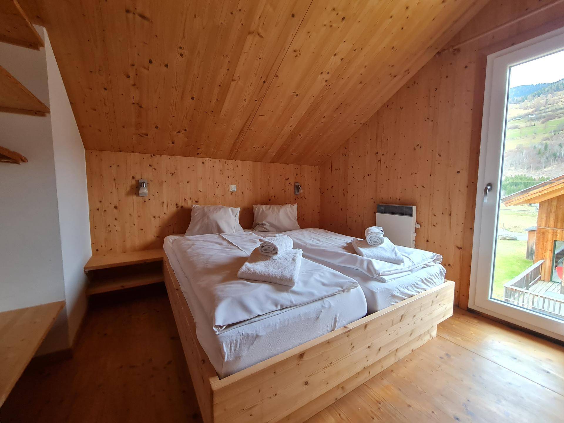 Geräumiges Schlafzimmer mit Holzmöbeln, Dachschräge und Fenster mit grüner Aussicht.