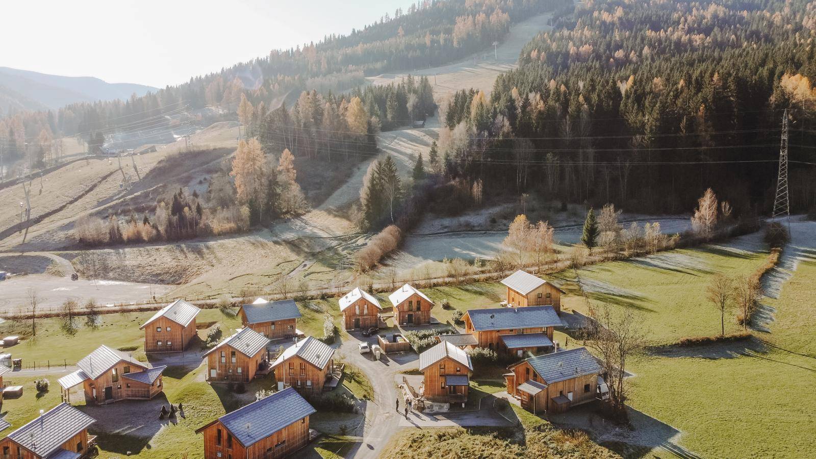 Weitläufige Luftaufnahme einer Feriensiedlung mit Holzhäusern in einer malerischen Berglandschaft.