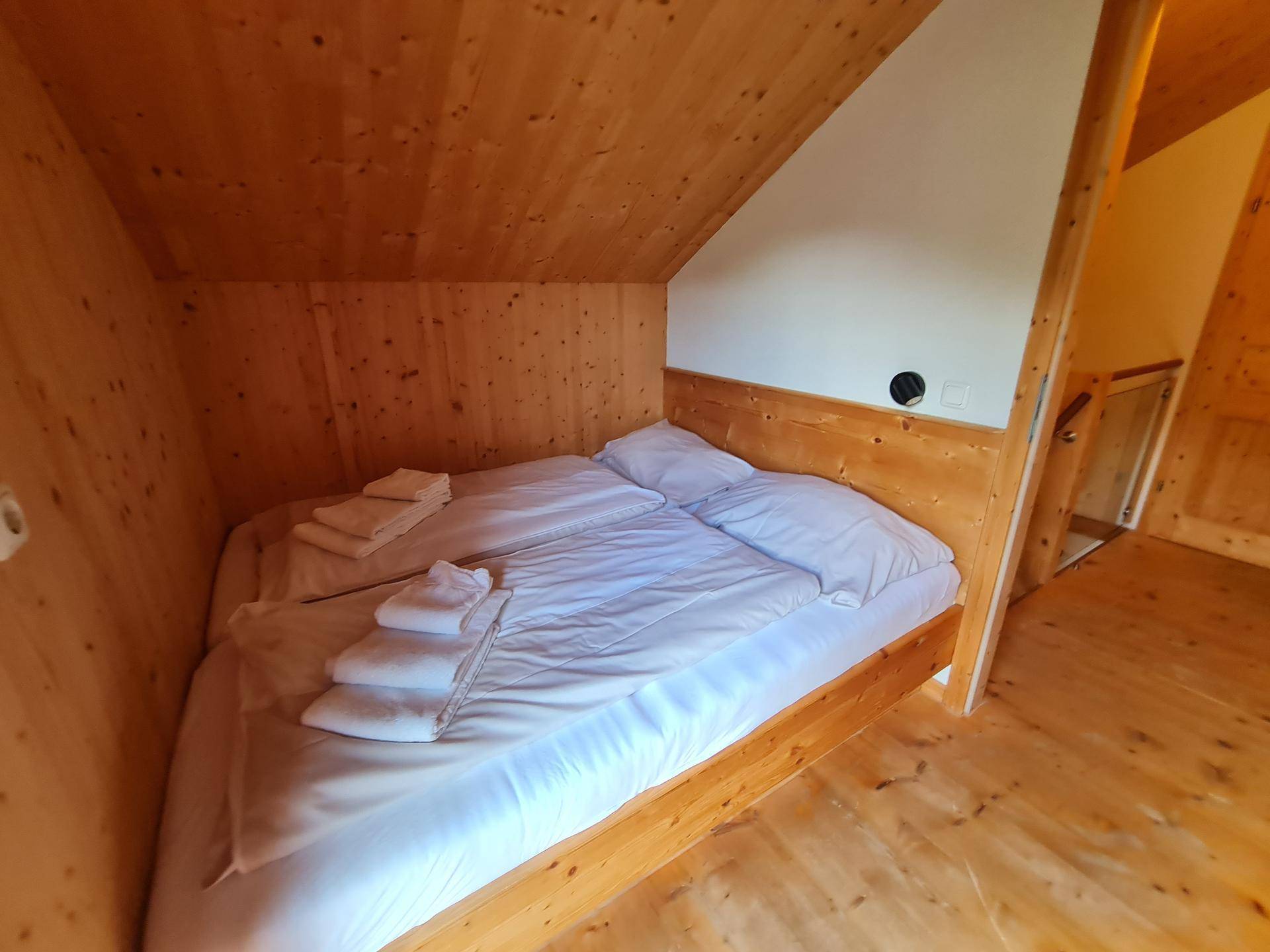 Schlafzimmer mit Holzbett, weißen Laken und rustikalem Holzinterieur im Dachgeschoss.
