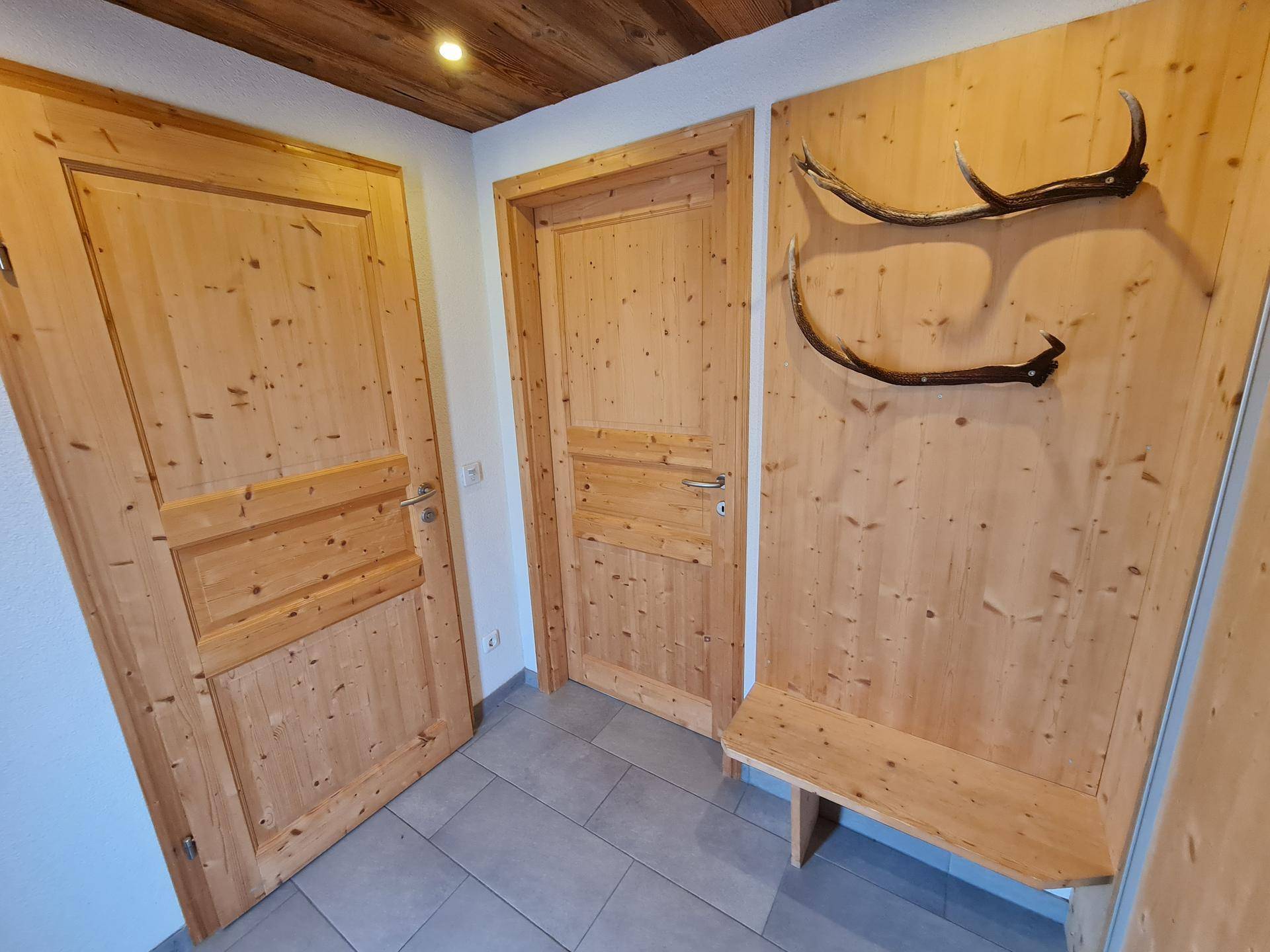 Heller Flur mit Holztüren, Fliesenboden und alpiner Geweihdekoration an der Wand.