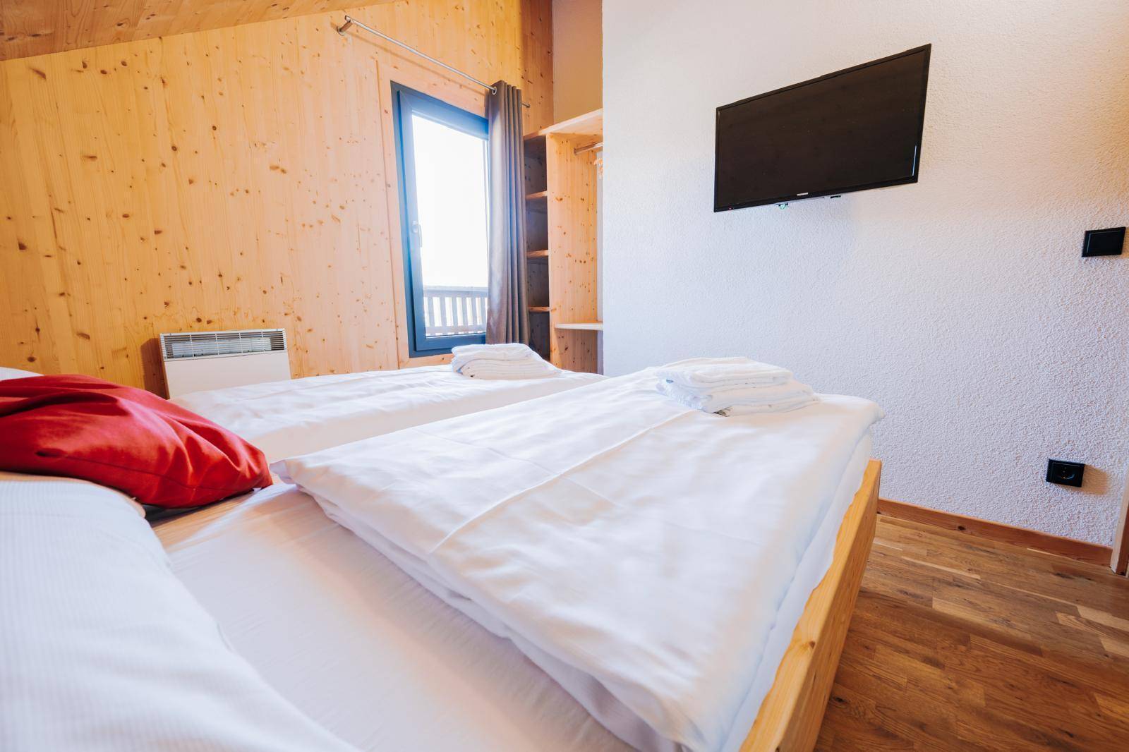 Helles Schlafzimmer mit zwei Einzelbetten, Holzboden und einem Flachbildfernseher.