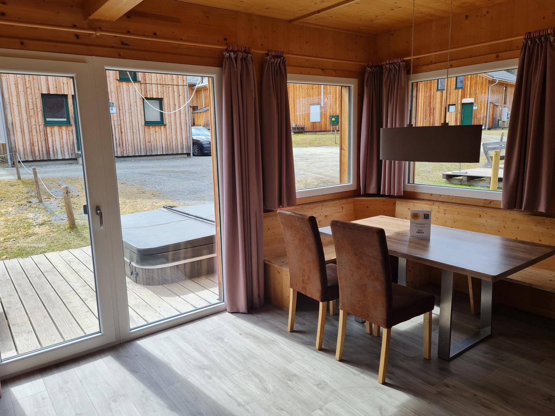 Gemütlicher Essbereich mit Holztisch, Sitzbank und Blick auf die Terrasse mit Whirlpool.