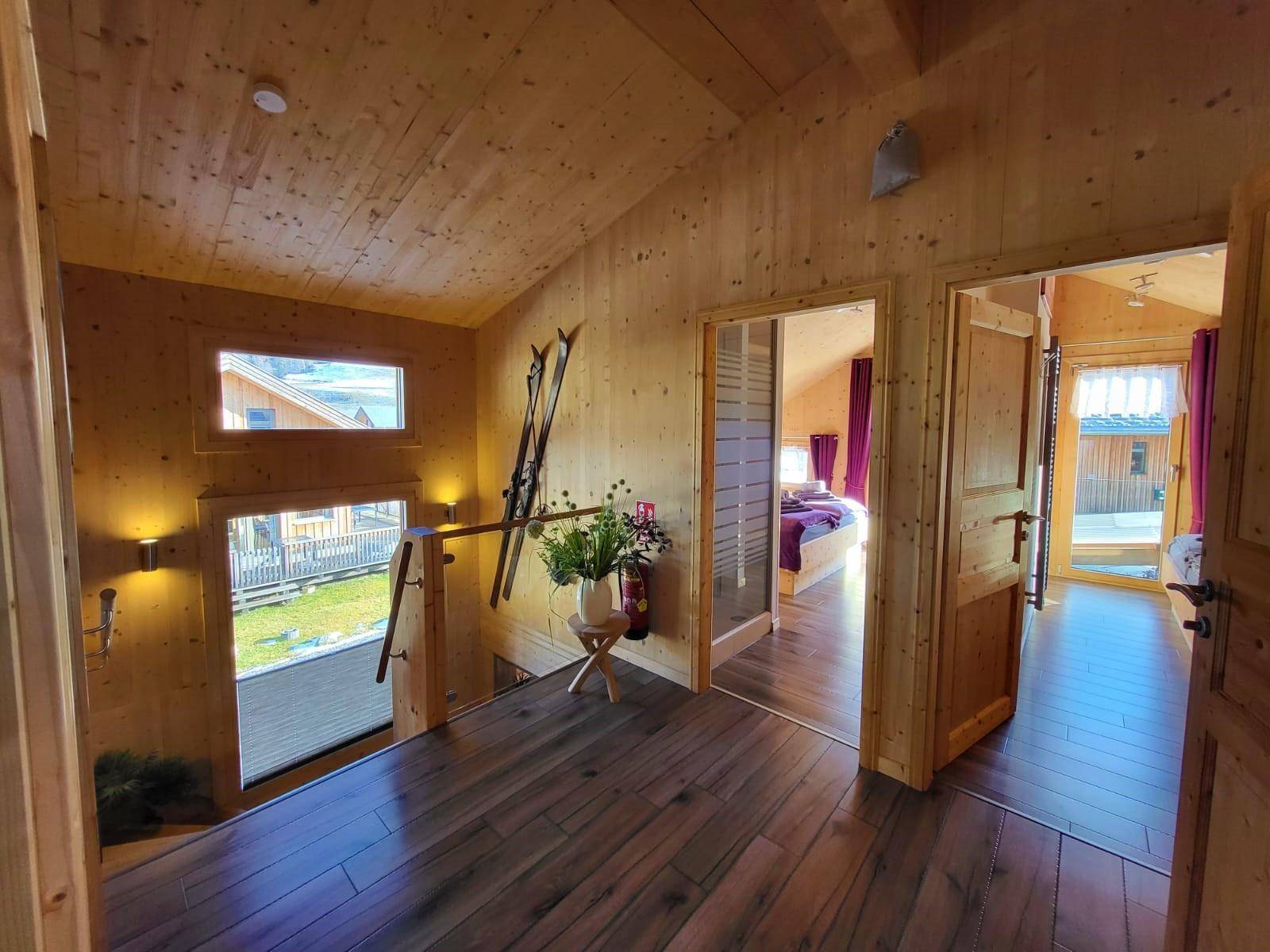 Heller Flur im Obergeschoss mit Holzwänden, Holzboden und Blick nach draußen.
