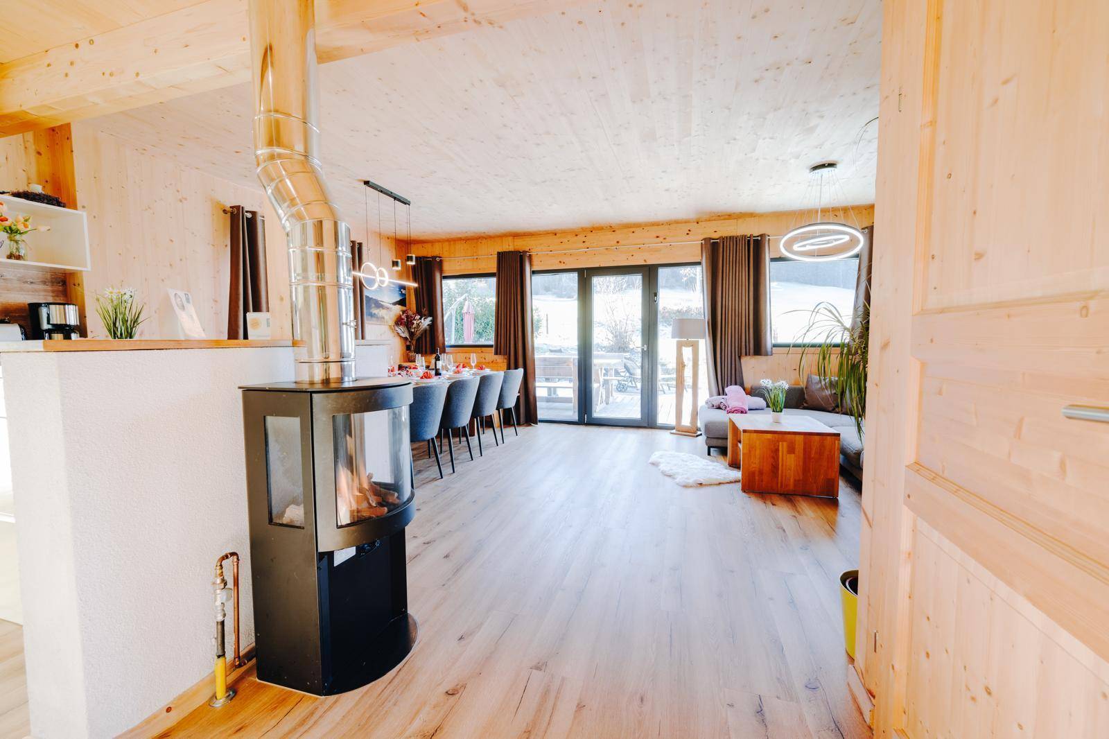 Offener Wohn- und Essbereich mit Holzboden, Kaminofen und Zugang zur Terrasse.