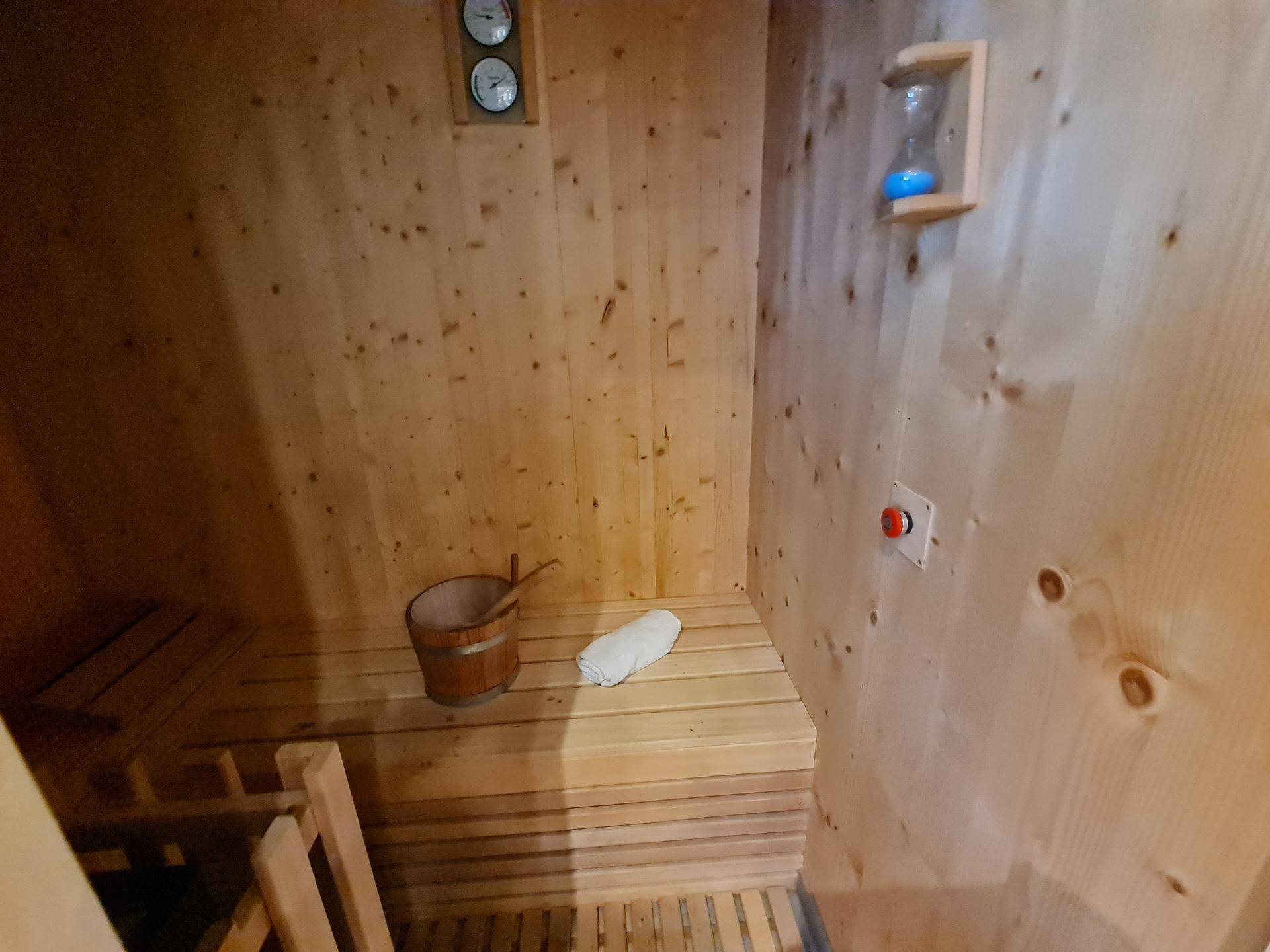 Innenansicht einer Holzsauna mit Heizofen, Bänken und Temperaturanzeigen an der Wand.