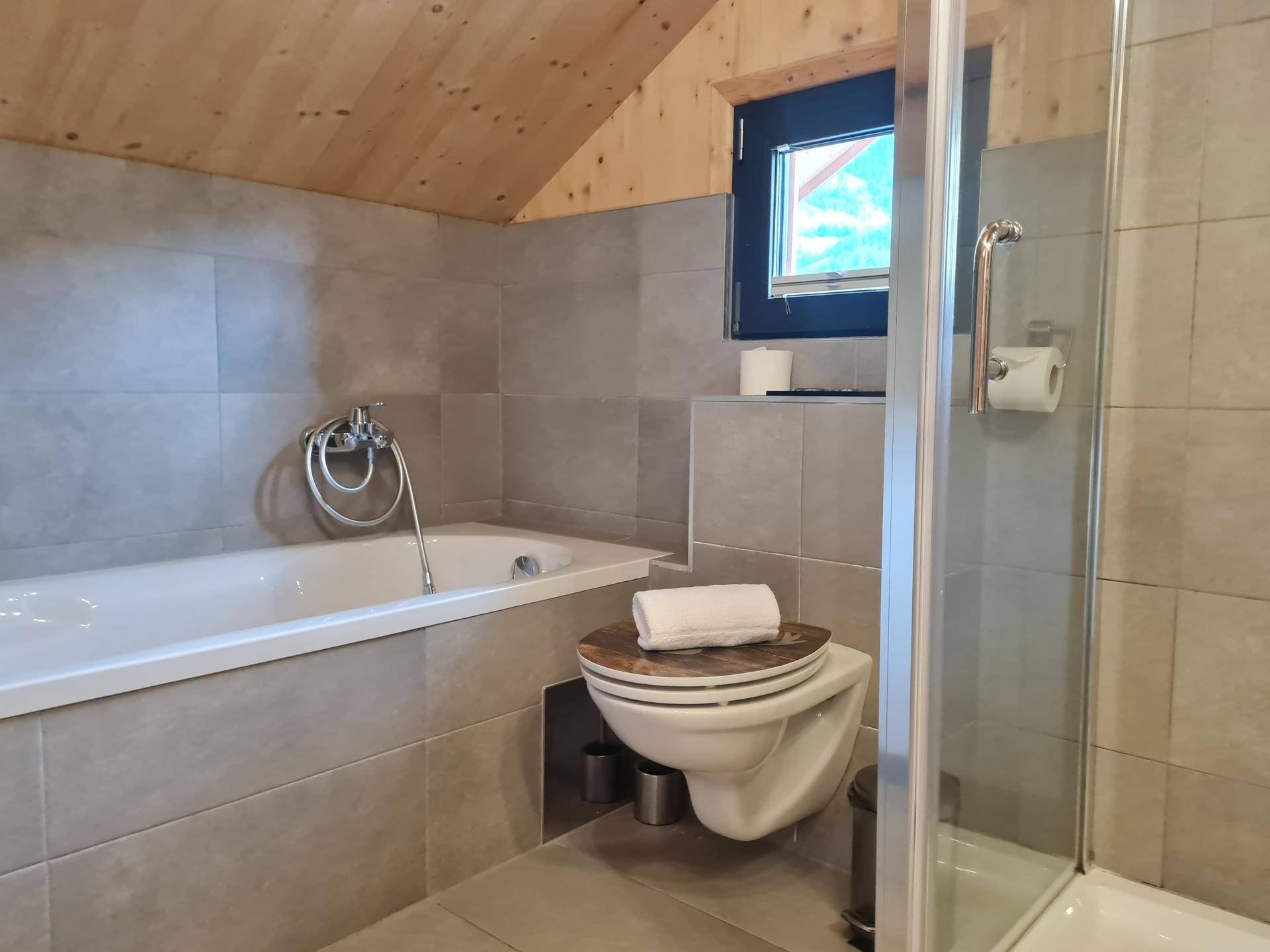 Modernes Badezimmer im Dachgeschoss mit Badewanne, Dusche und Fliesenboden.