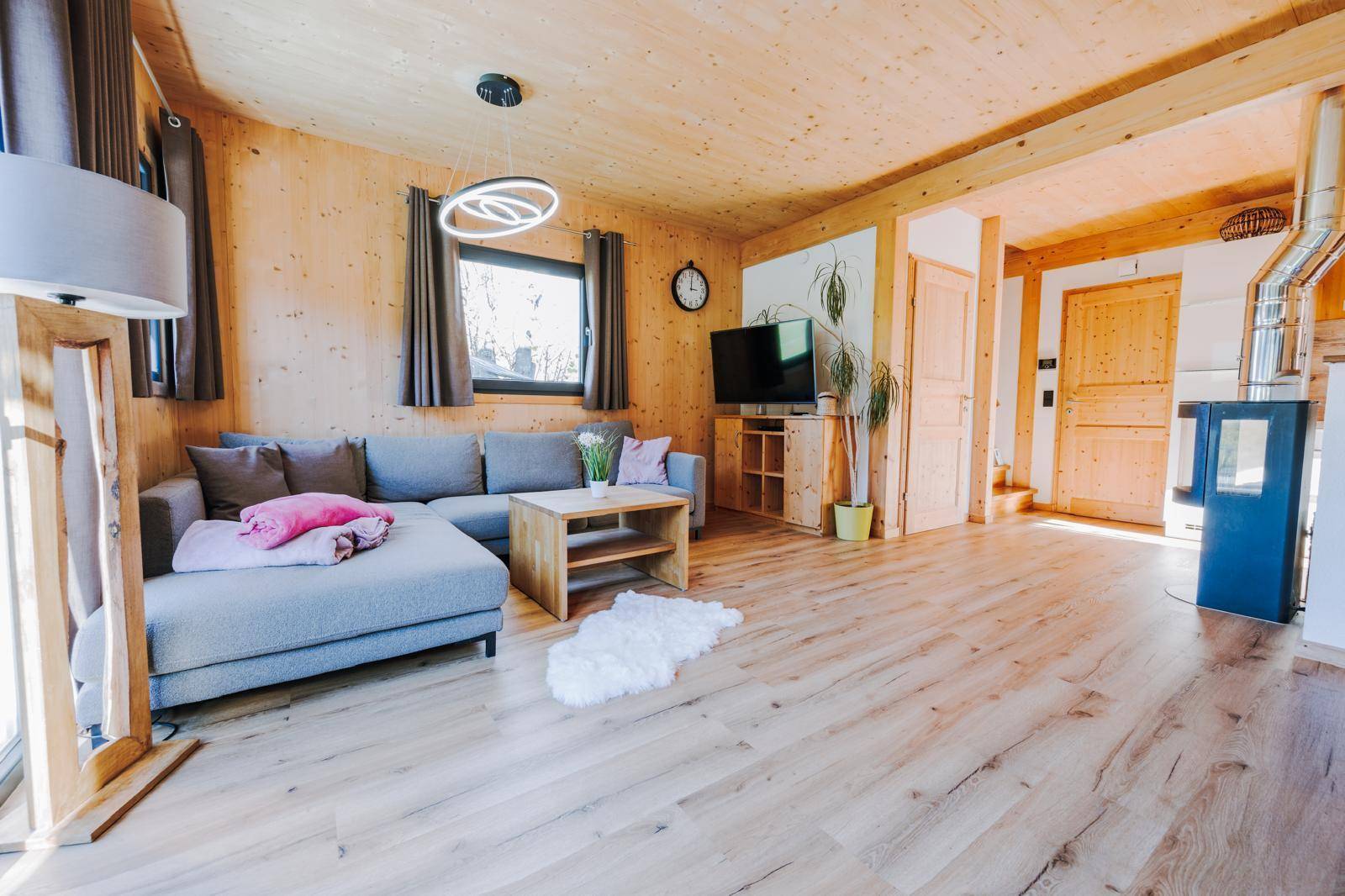 Gemütliches Wohnzimmer mit Ecksofa, Holzboden und einem modernen Kaminofen.