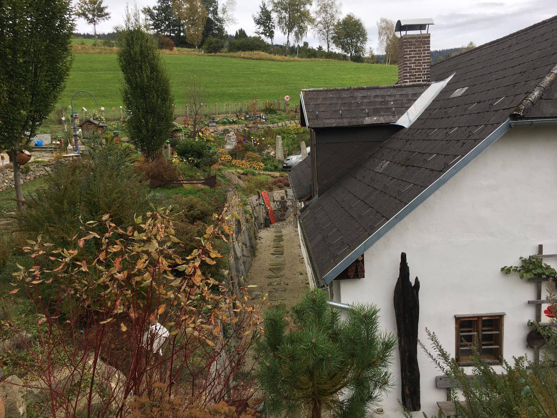 Seitenansicht des Hauses mit dunklem Dach, Schornstein und weitem Blick auf grüne Hügel.