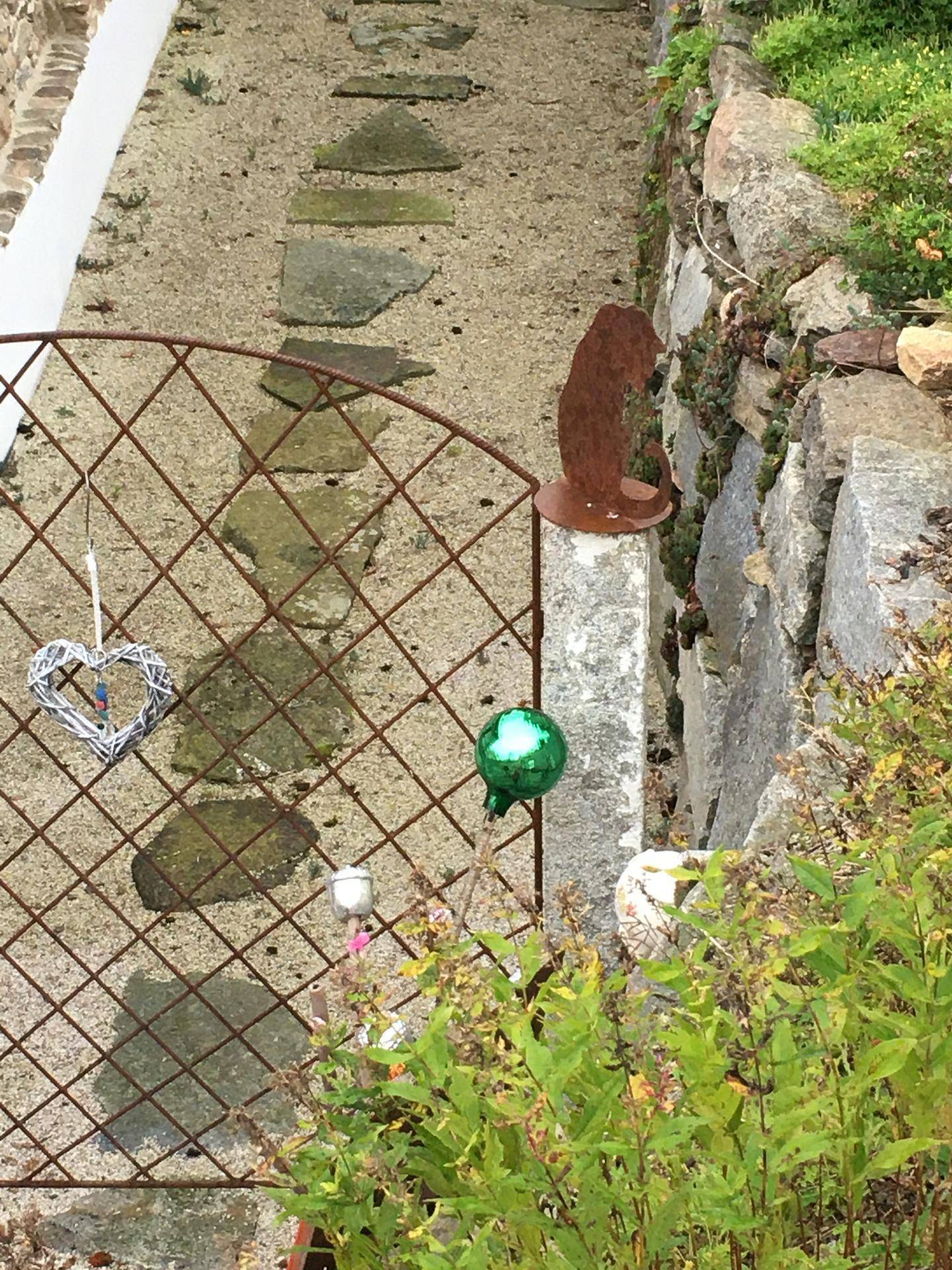 Dekoratives Metalltor mit Herzverzierung und Steintreppe in einem naturnahen Gartenbereich.