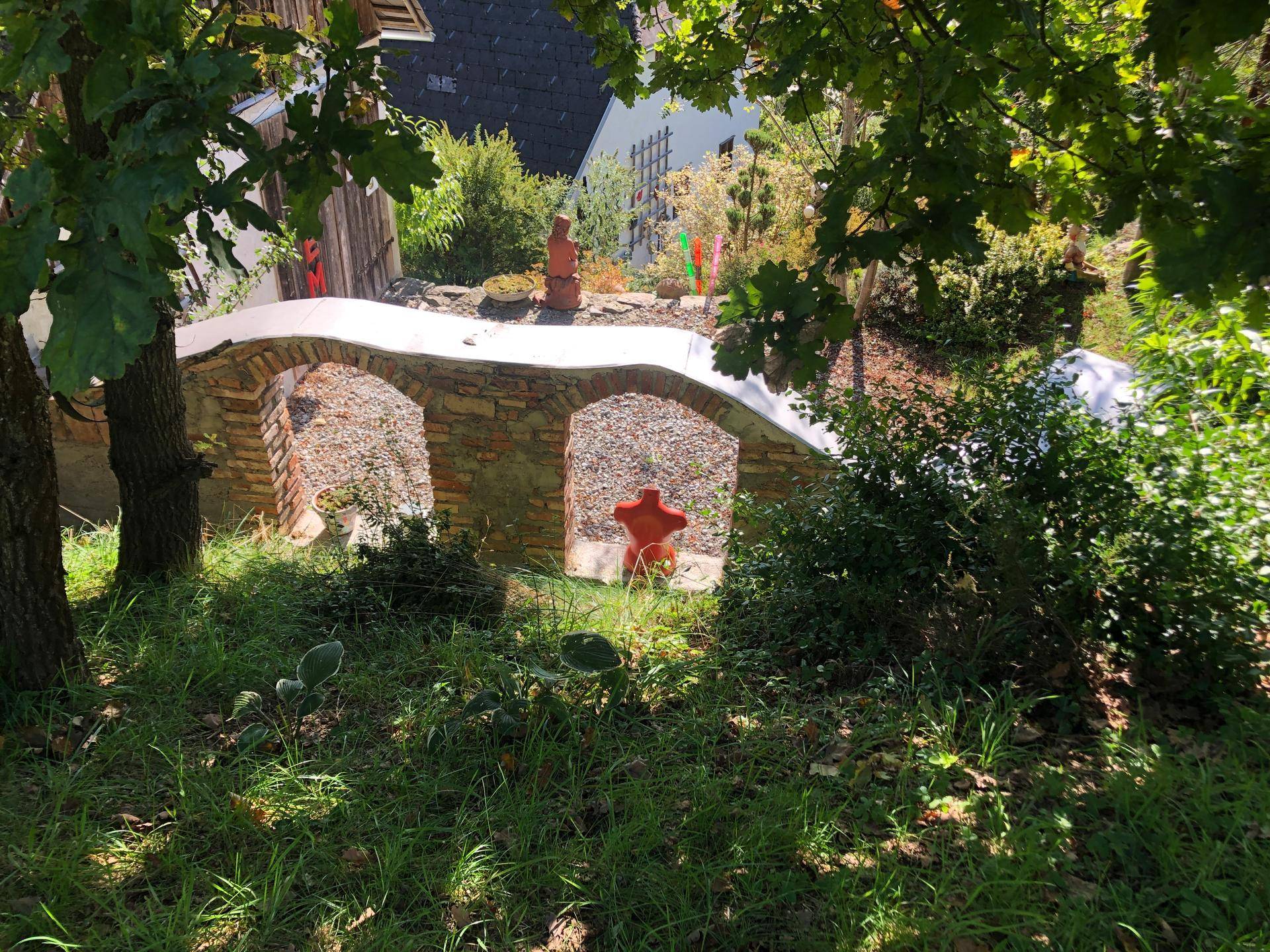 Dekorative Steinbogenstruktur in einem naturbelassenen Garten mit viel Grün.