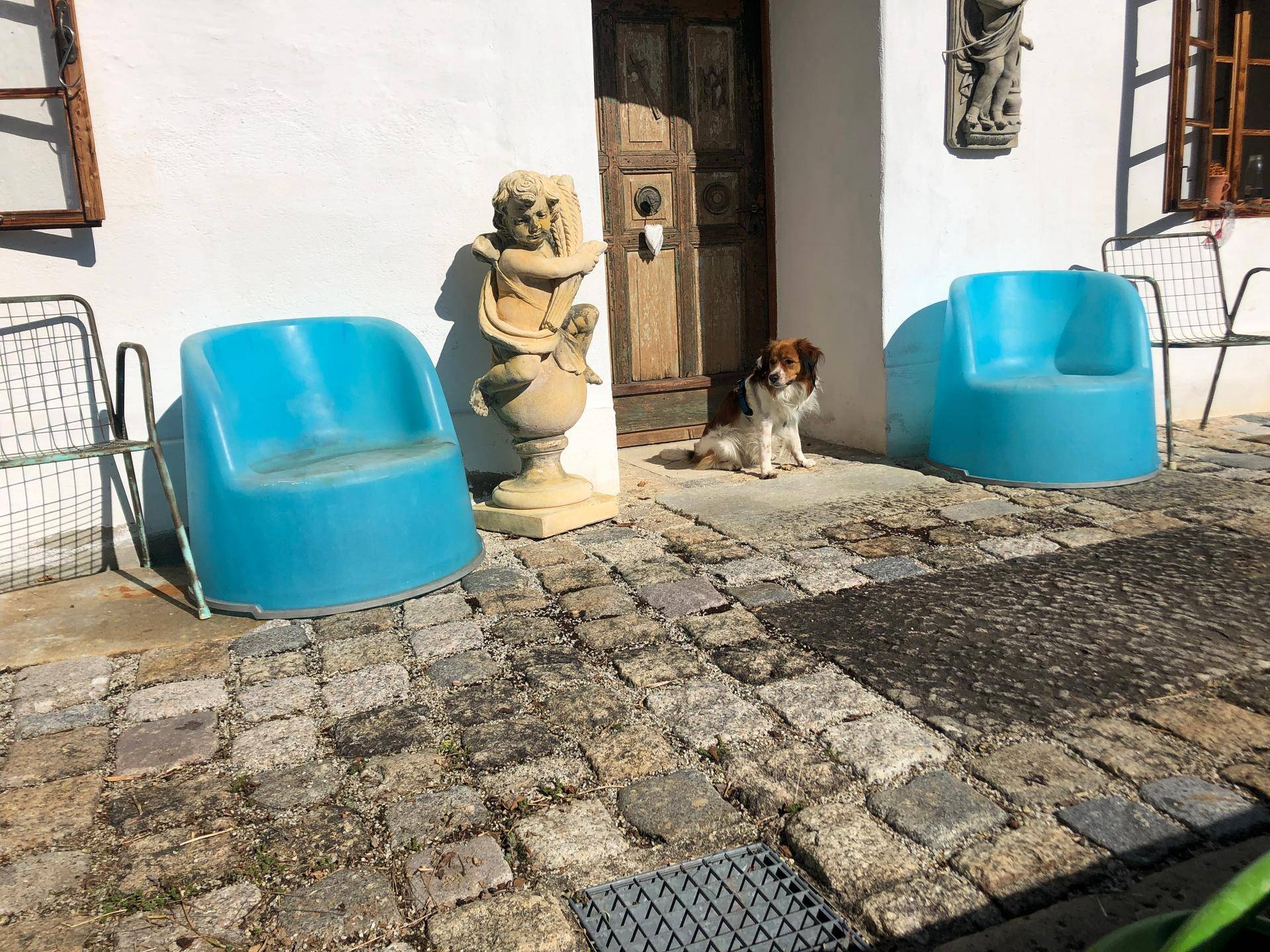 Eingangsbereich mit rustikaler Holztür, blauen Stühlen und einer dekorativen Statue.