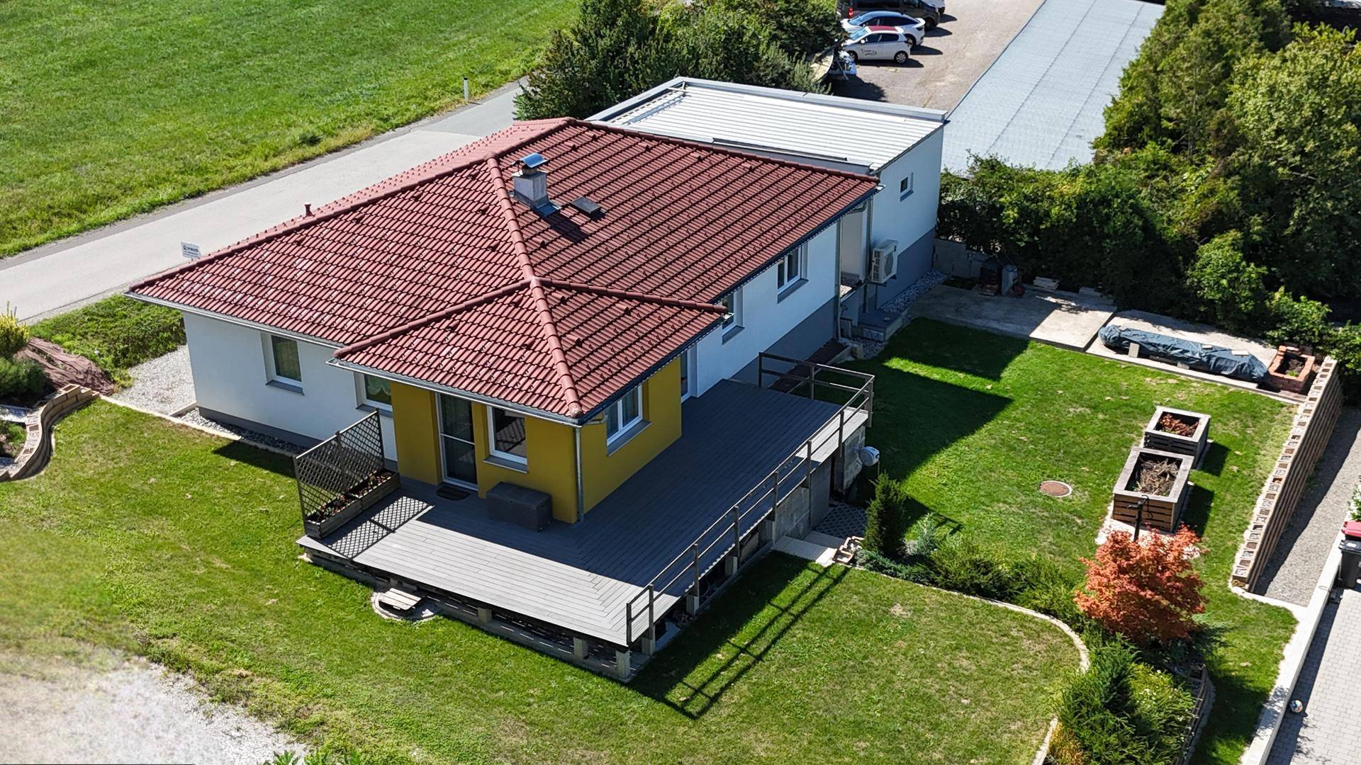 Rückansicht des Hauses mit großer Holzterrasse und gepflegtem Gartenbereich.