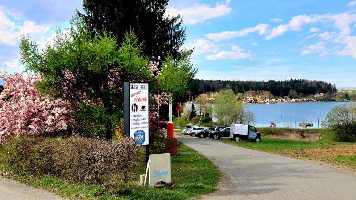 Zufahrtsweg zum See mit Restaurant-Schild und parkenden Autos.