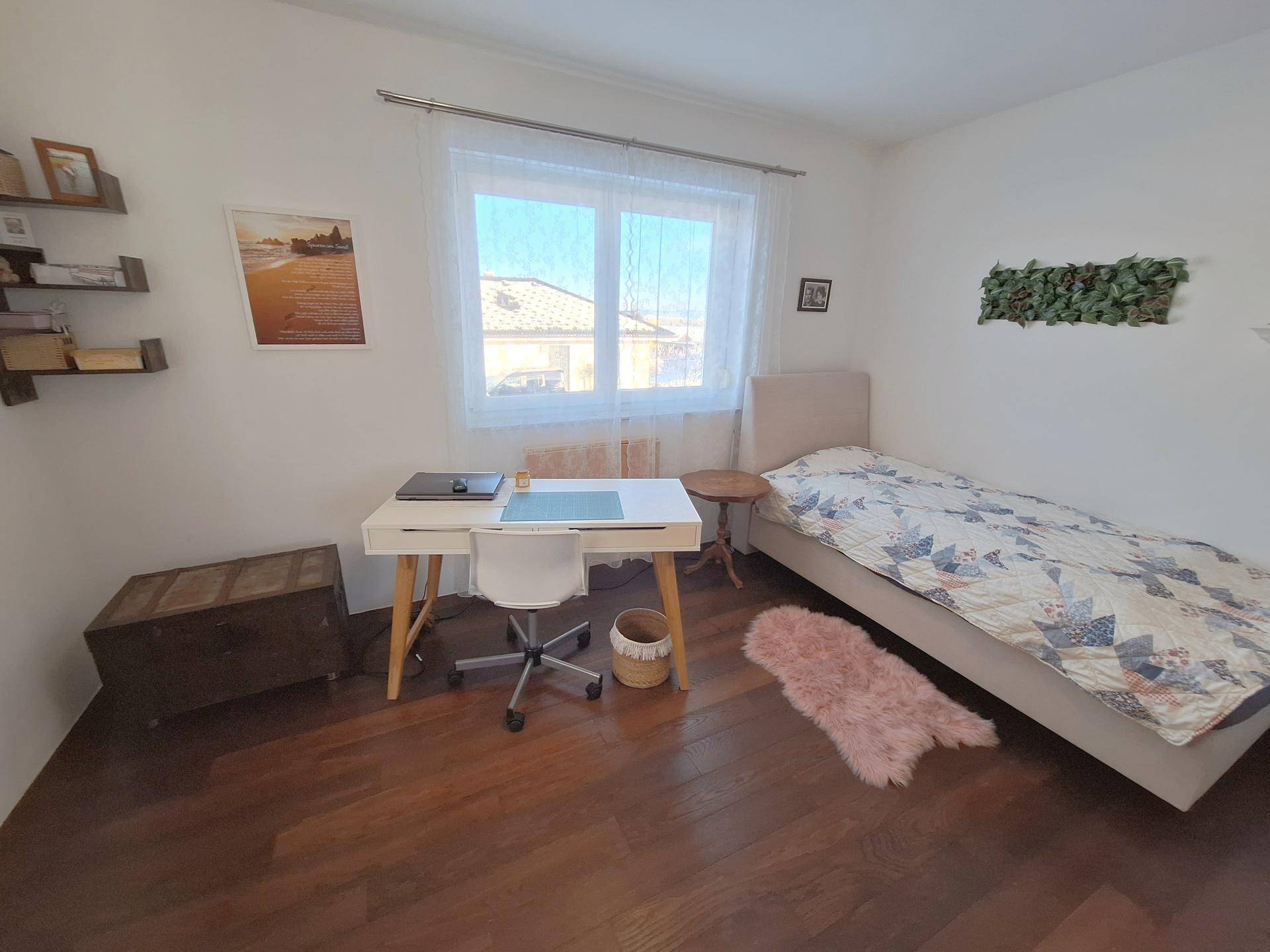 Helles Schlafzimmer mit Einzelbett, Schreibtisch und Holzboden.