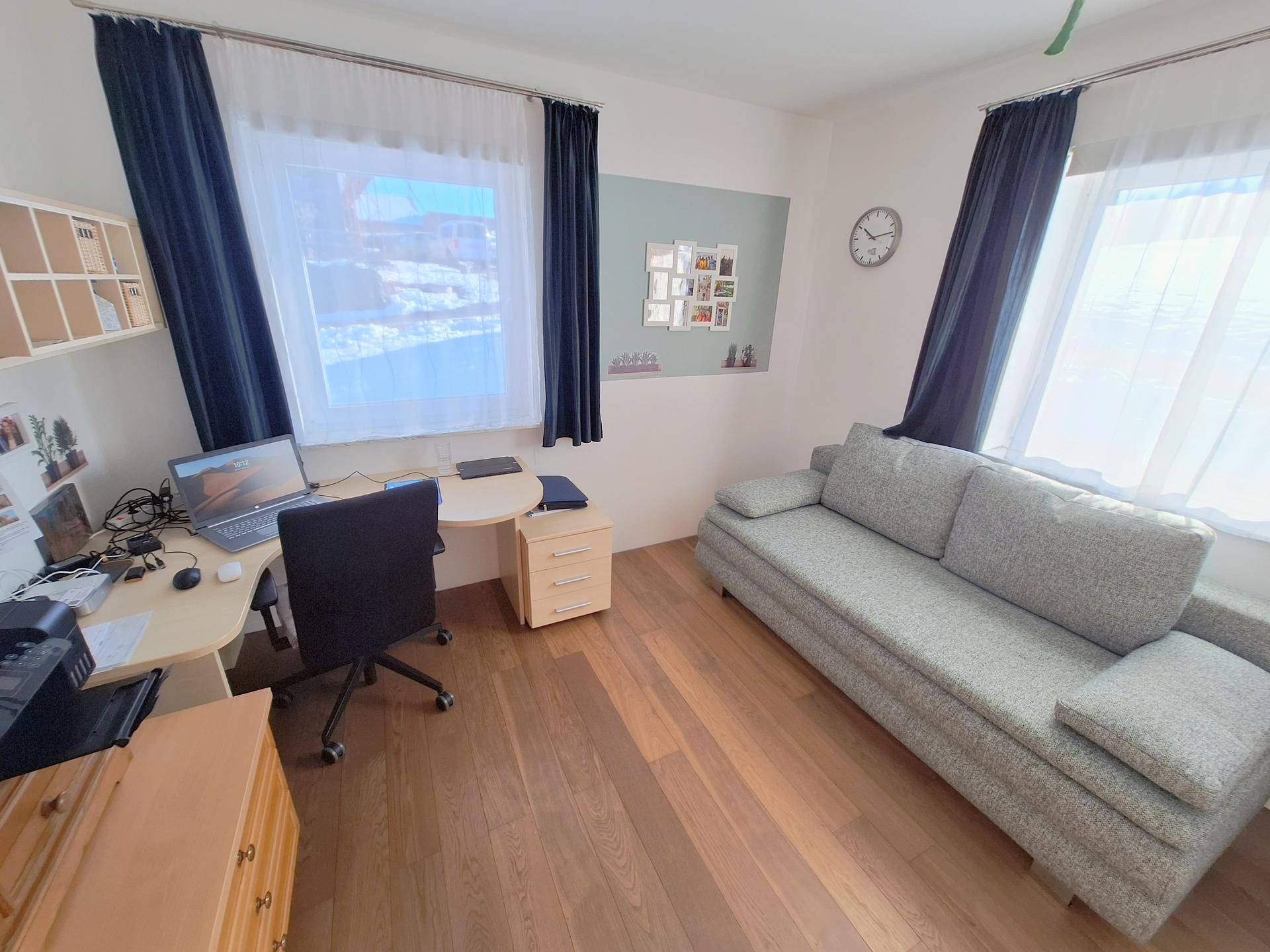 Arbeitszimmer mit Schreibtisch, Sofa und großen Fenstern für viel Tageslicht.