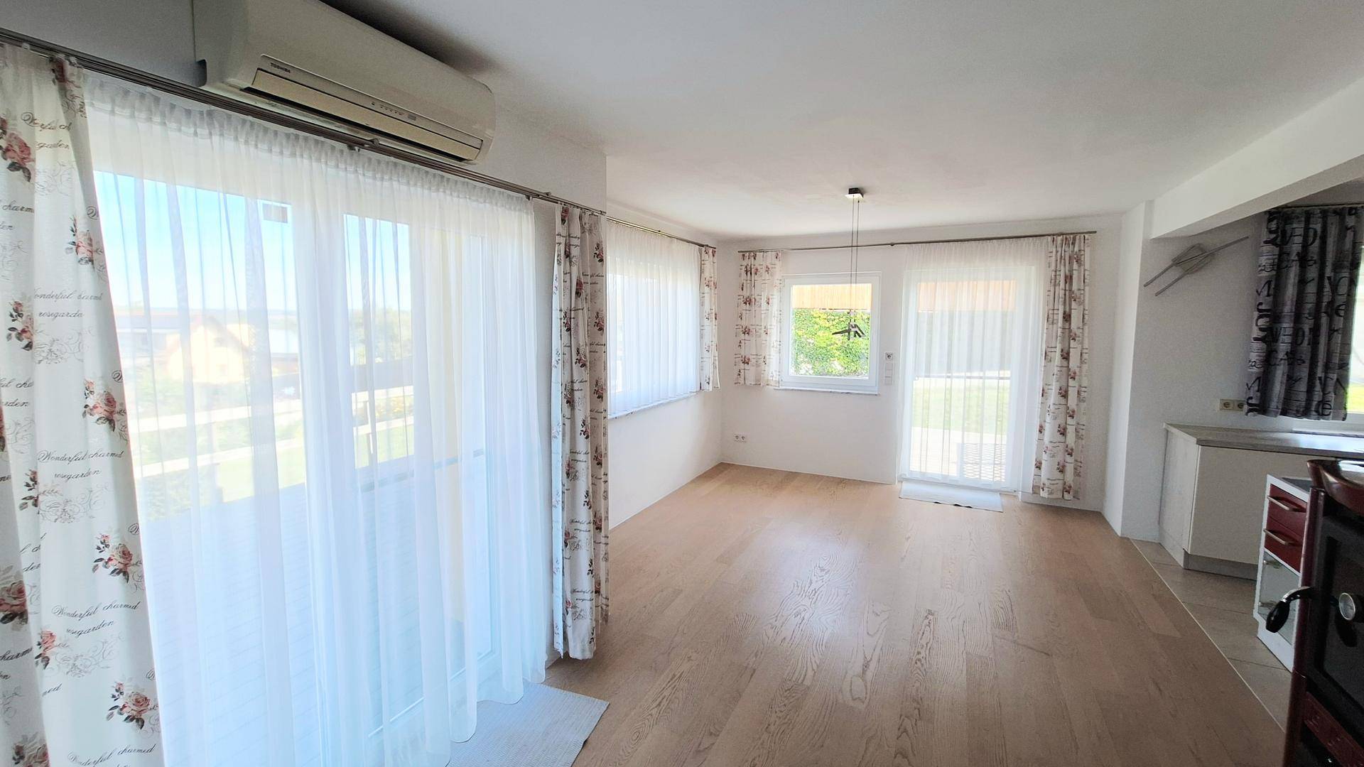 Helles Wohnzimmer mit großen Fenstern, Vorhängen und Klimaanlage.