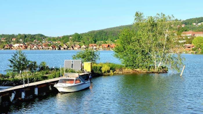 Boot am Steg auf dem See mit grüner Uferlandschaft im Hintergrund.