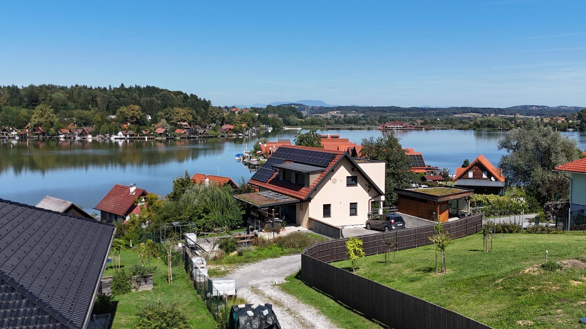 Luftaufnahme von Häusern am Seeufer mit Solaranlagen auf den Dächern und Bergblick.