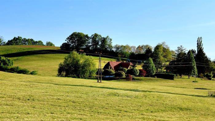 Haus eingebettet in eine weite, grüne Hügellandschaft unter blauem Himmel.