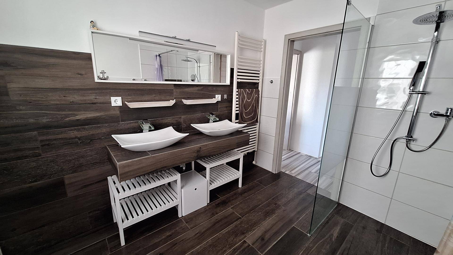 Modernes Badezimmer mit Doppelwaschbecken, begehbarer Dusche und dunklen Holzfliesen.