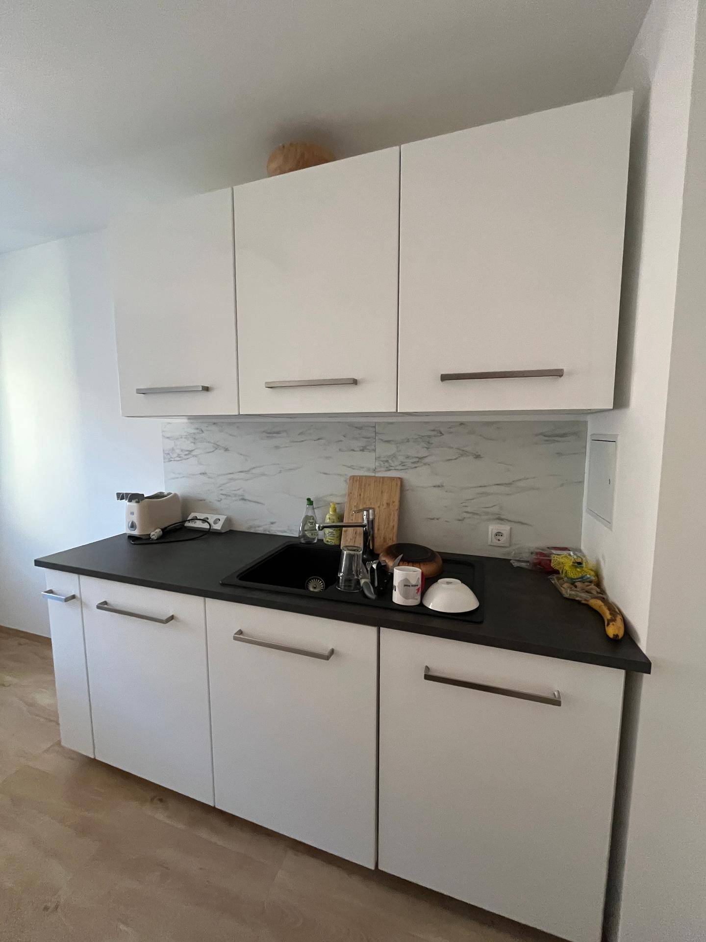 Weiße Küchenschränke mit dunkler Arbeitsplatte und Spüle, ergänzt durch eine helle Rückwand.