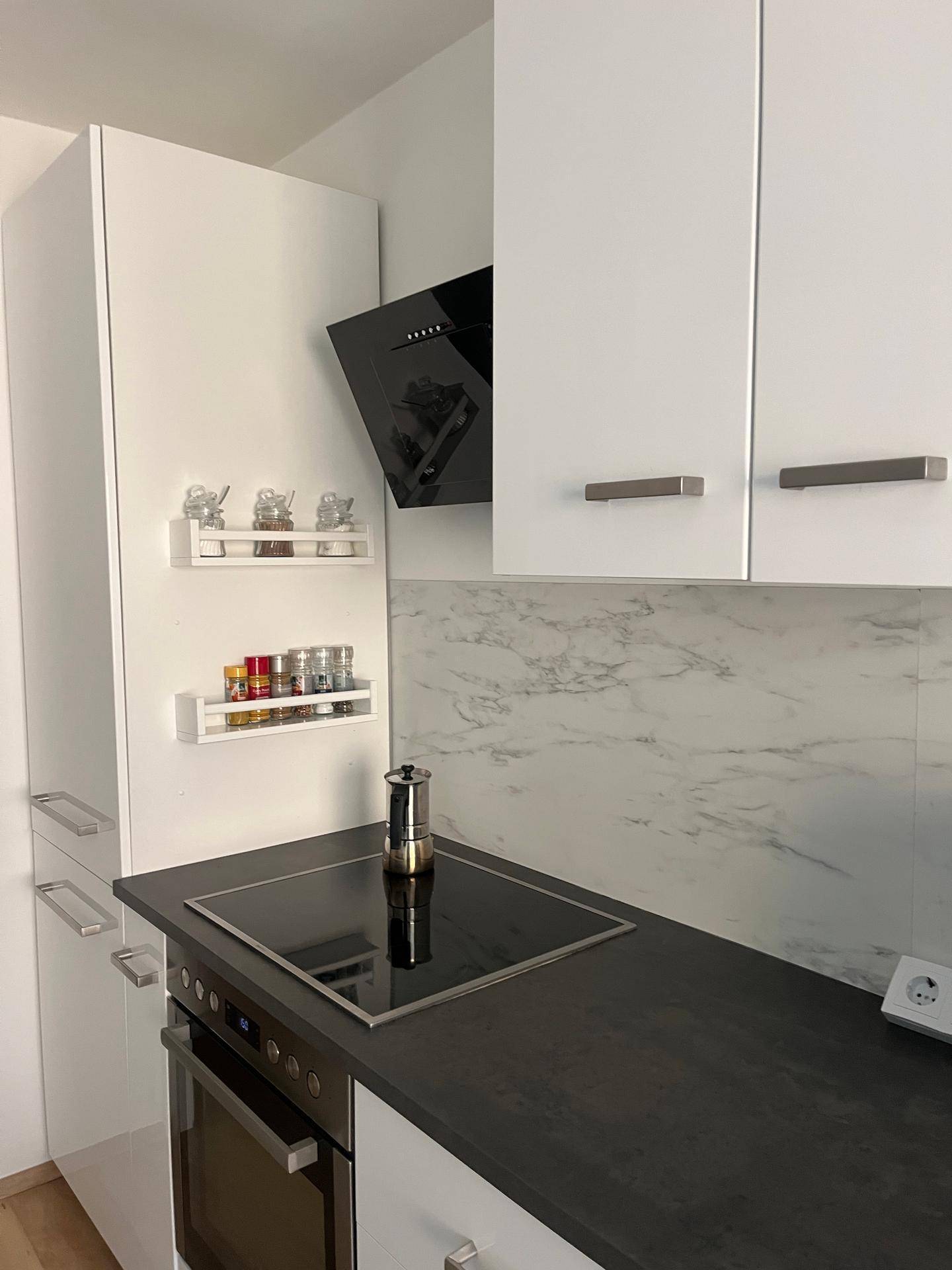 Moderne Küchenzeile mit Induktionskochfeld, Backofen und praktischen Gewürzregalen an der Wand.