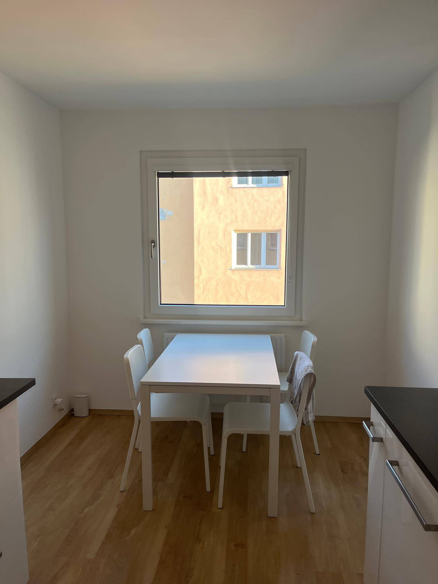 Essbereich in der Küche mit einem schlichten weißen Tisch und Stühlen vor einem Fenster.