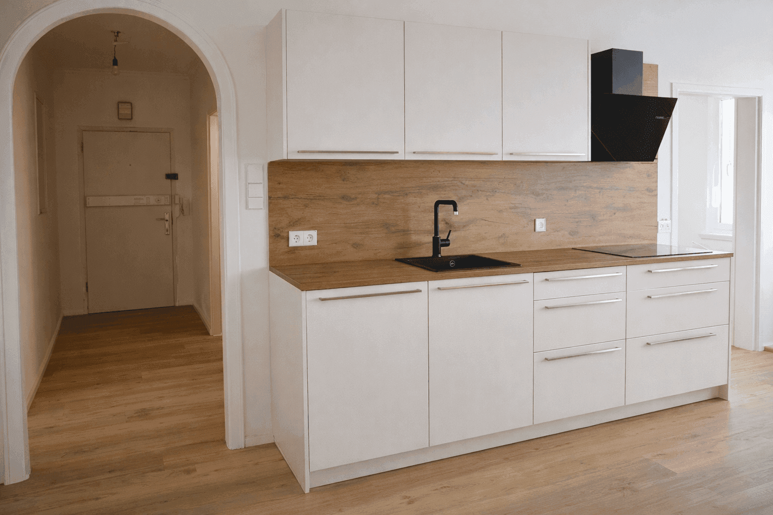 Moderne Küchenzeile mit weißen Hochglanzschränken, Holzarbeitsplatte und integriertem Induktionskochfeld.