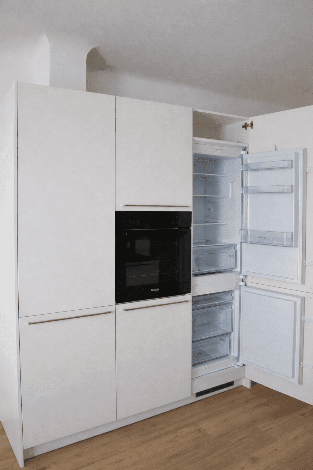 Integrierte Küchengeräte mit Backofen, Kühlschrank und Gefrierfach in weißen, grifflosem Hochschränken.